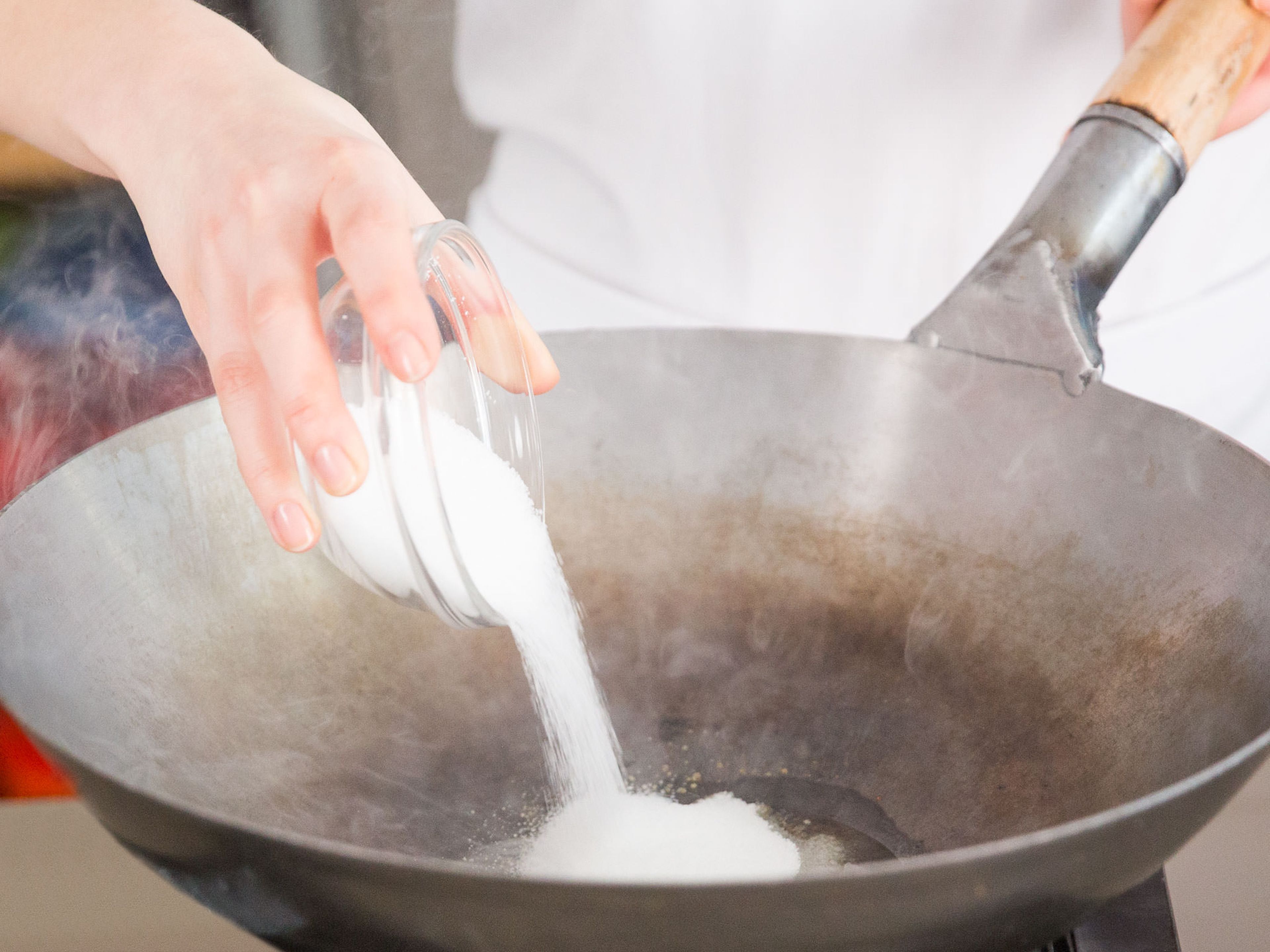 Pflanzenöl und Zucker in den Wok geben und bei schwacher Hitze 3 – 5 Min. kochen, bis der Zucker beginnt zu karamellisieren. Vorsichtig Wasser hinzugeben und das Karamell zu verdünnen. Karamell aus dem Wok nehmen und beiseitestellen.
