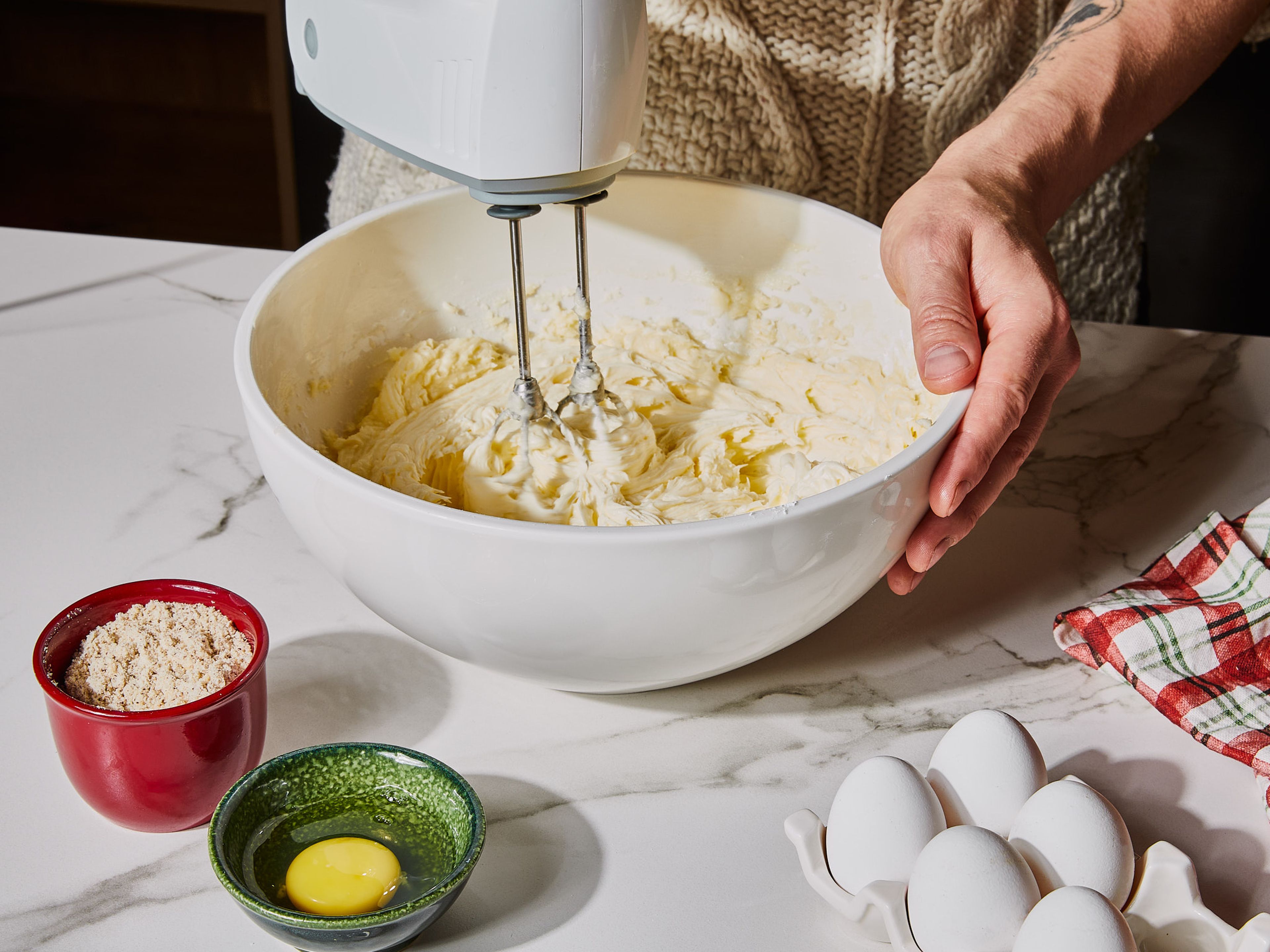 In einer großen Schüssel Butter und Puderzucker mit einem Handrührgerät schaumig schlagen. Ei und Eigelb hinzufügen und weiterschlagen, bis eine homogene Masse entsteht. Mehl und gemahlene Haselnüsse hineinsieben und sorgfältig unterheben, bis ein knetbarer Mürbeteig entsteht. Kurz beiseite stellen.