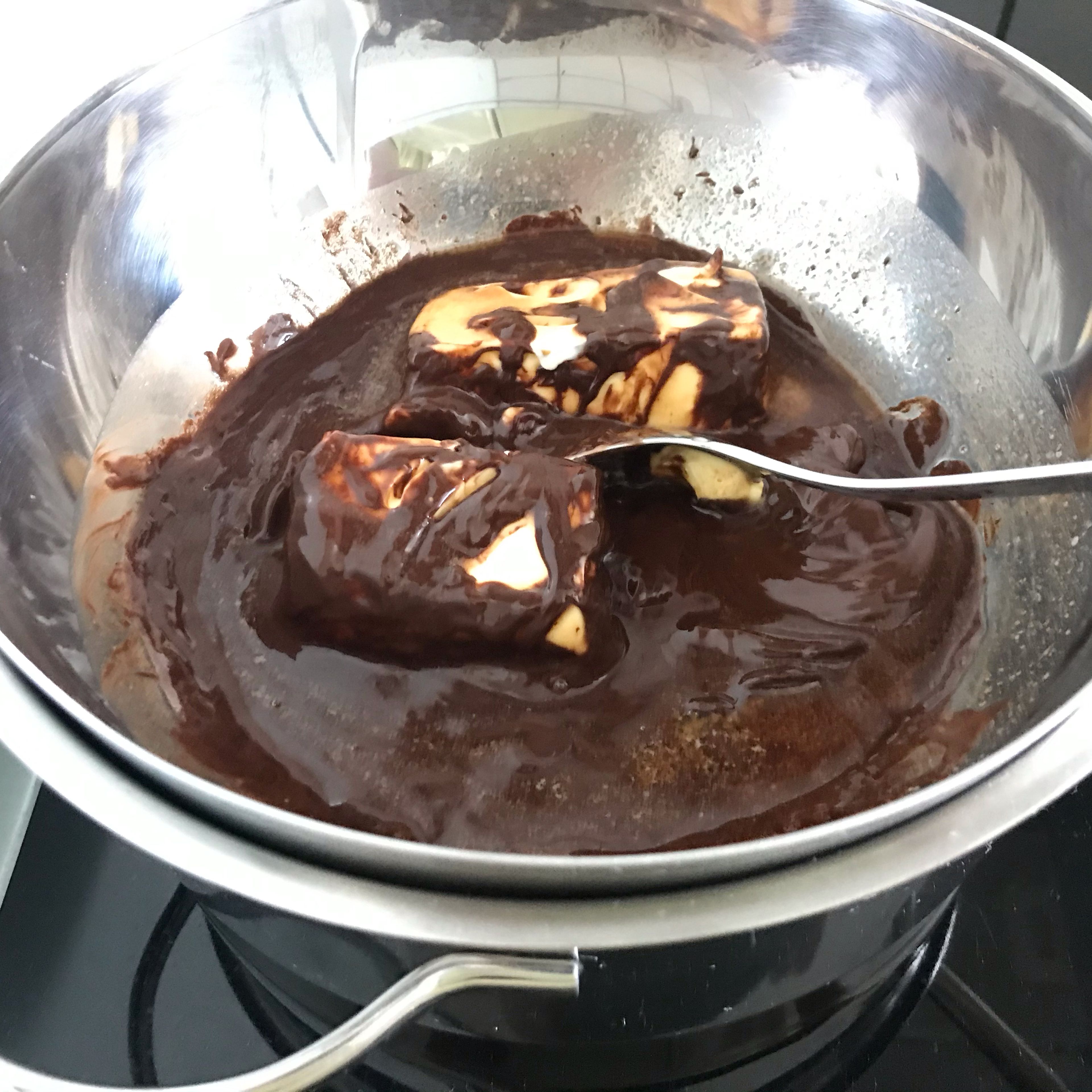 Währenddessen die Butter in kleinen Stücken schneiden und zu der geschmolzenen Schokolade geben und verrühren.