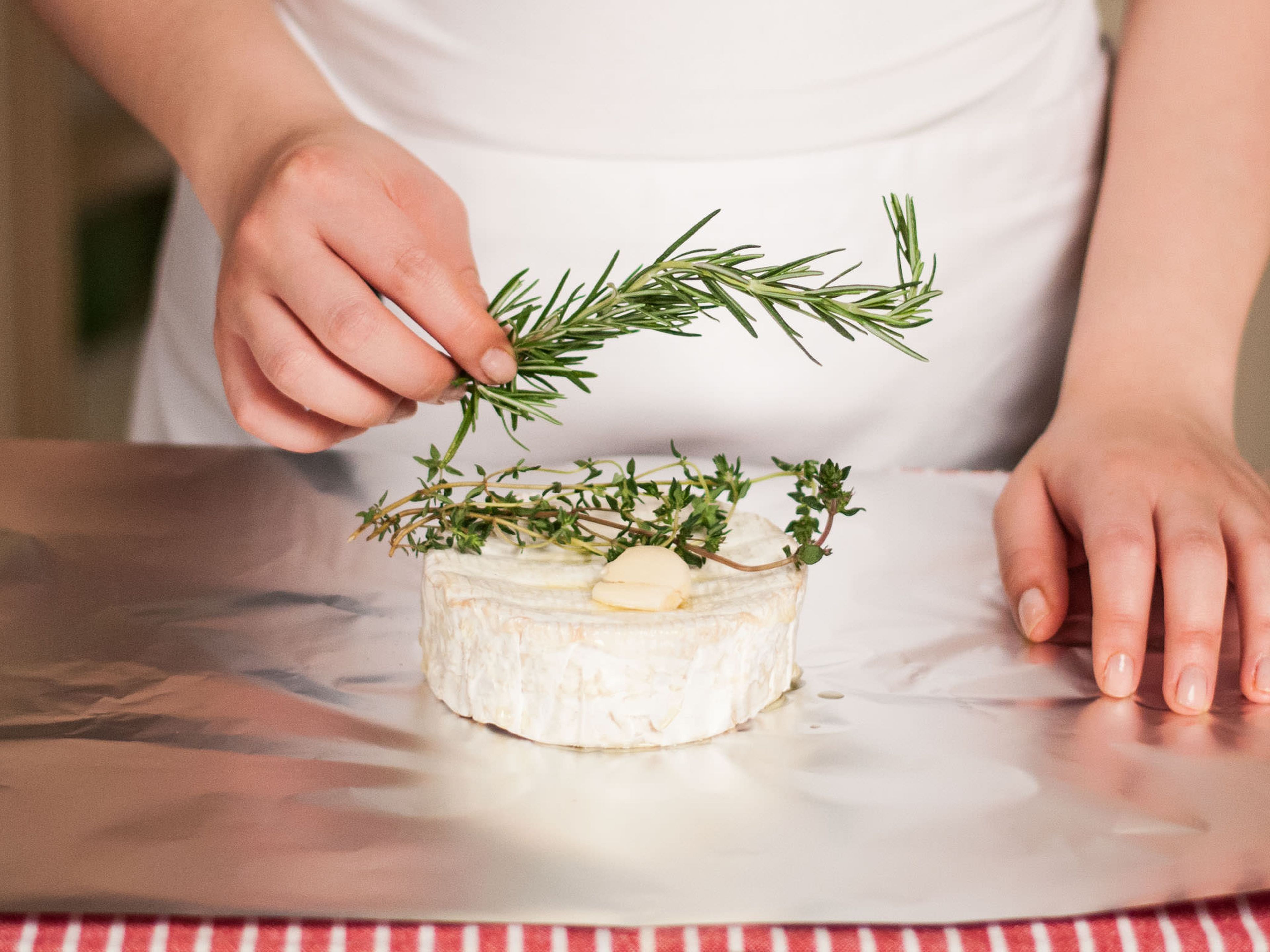 Preheat the grill. Place camembert on a square of aluminum foil and brush it with some olive oil. Top with sprigs of rosemary, thyme and crushed garlic clove.