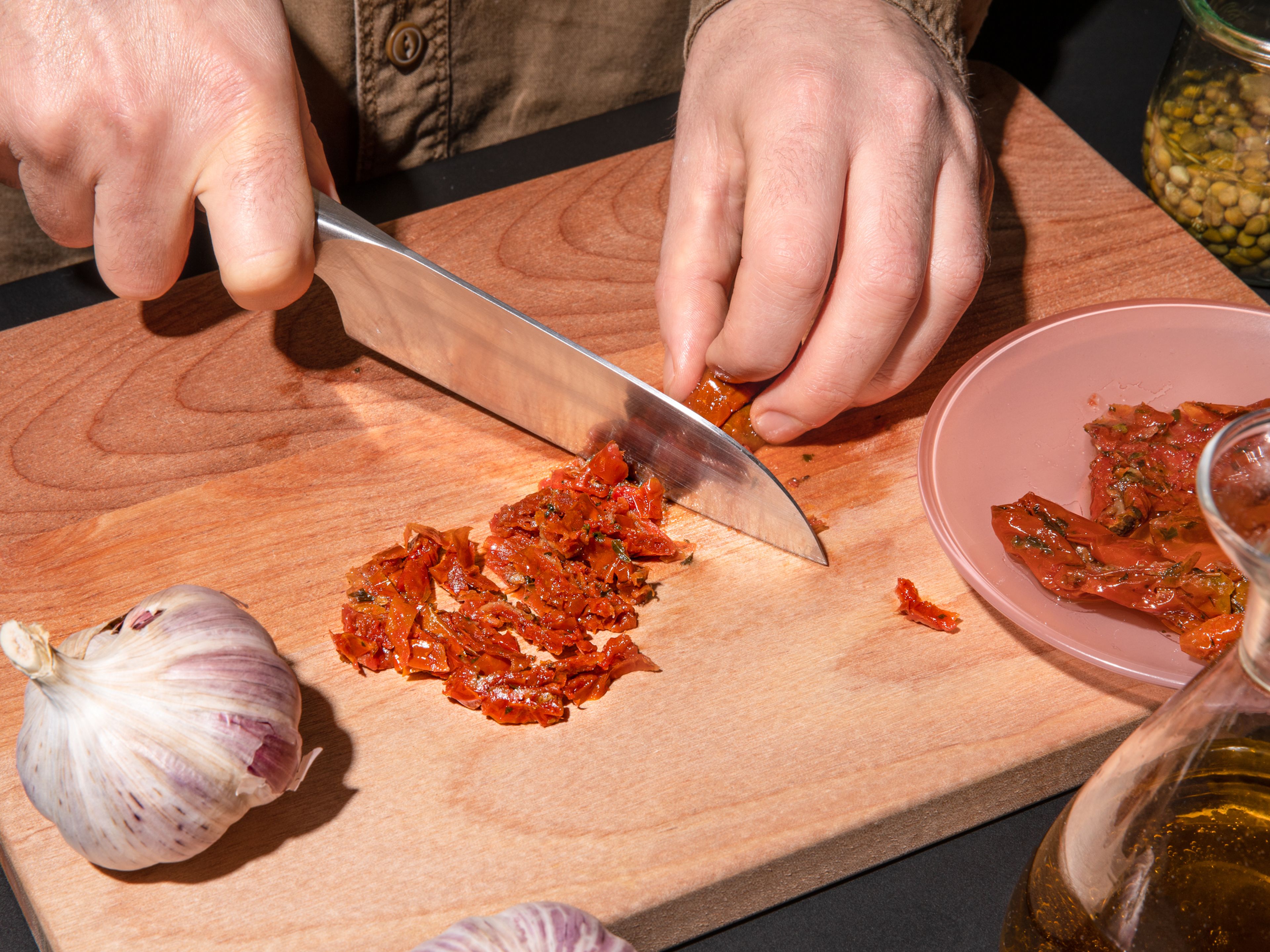 Backofen auf 180°C vorheizen. Frischkäse aus dem Kühlschrank nehmen, damit er bei Zimmertemperatur weich wird. In der Zwischenzeit die getrockneten Tomaten abtropfen lassen und in dünne Streifen schneiden, die Kapern abtropfen lassen und mit einem Küchentuch trocknen und den Knoblauch in dünne Scheiben schneiden. Das Ciabatta in dünne Scheiben schneiden und den Basilikum hacken.