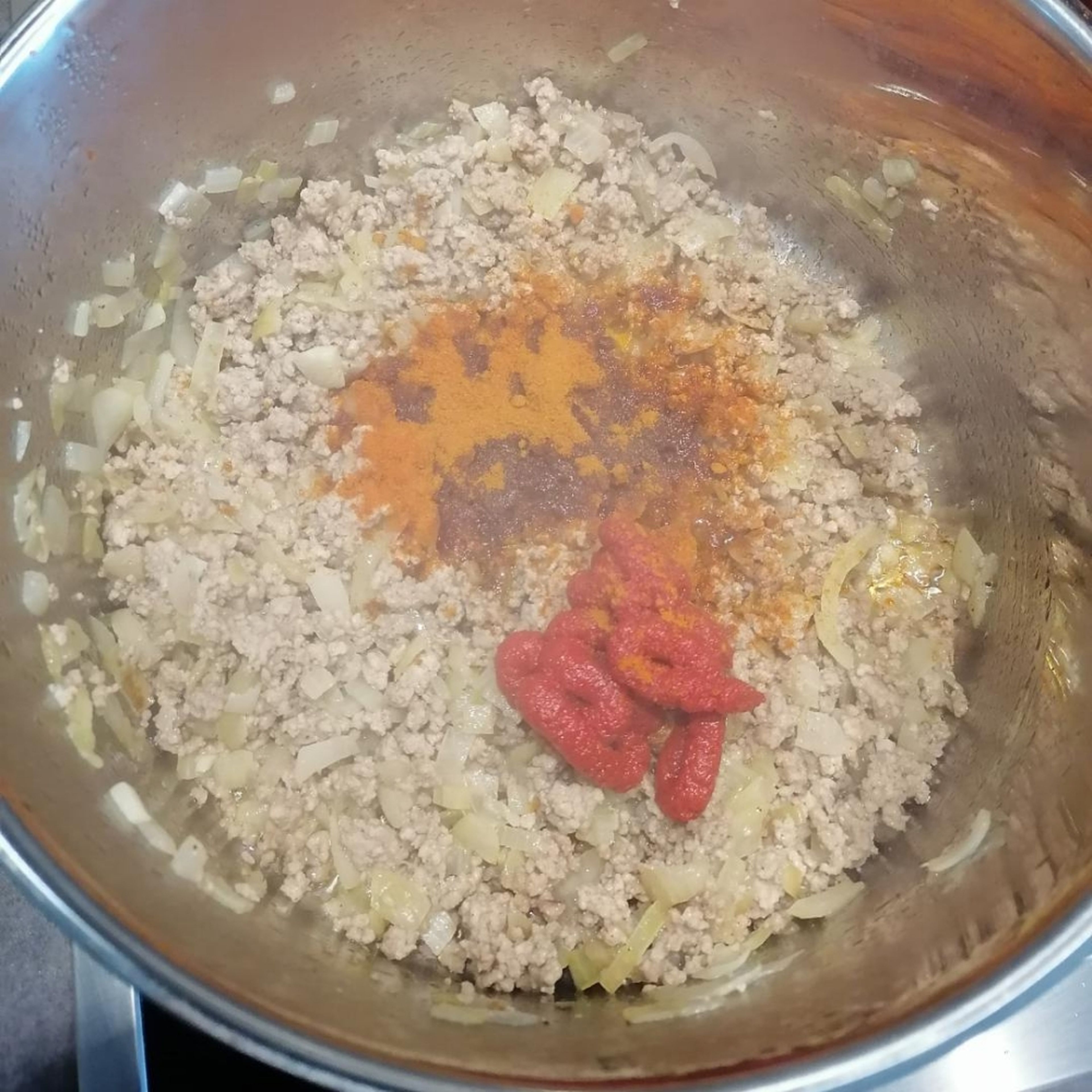 Wenn das Hack krümelig gebraten ist, der Mischung Tomatenmark und Gewürze hinzufügen.