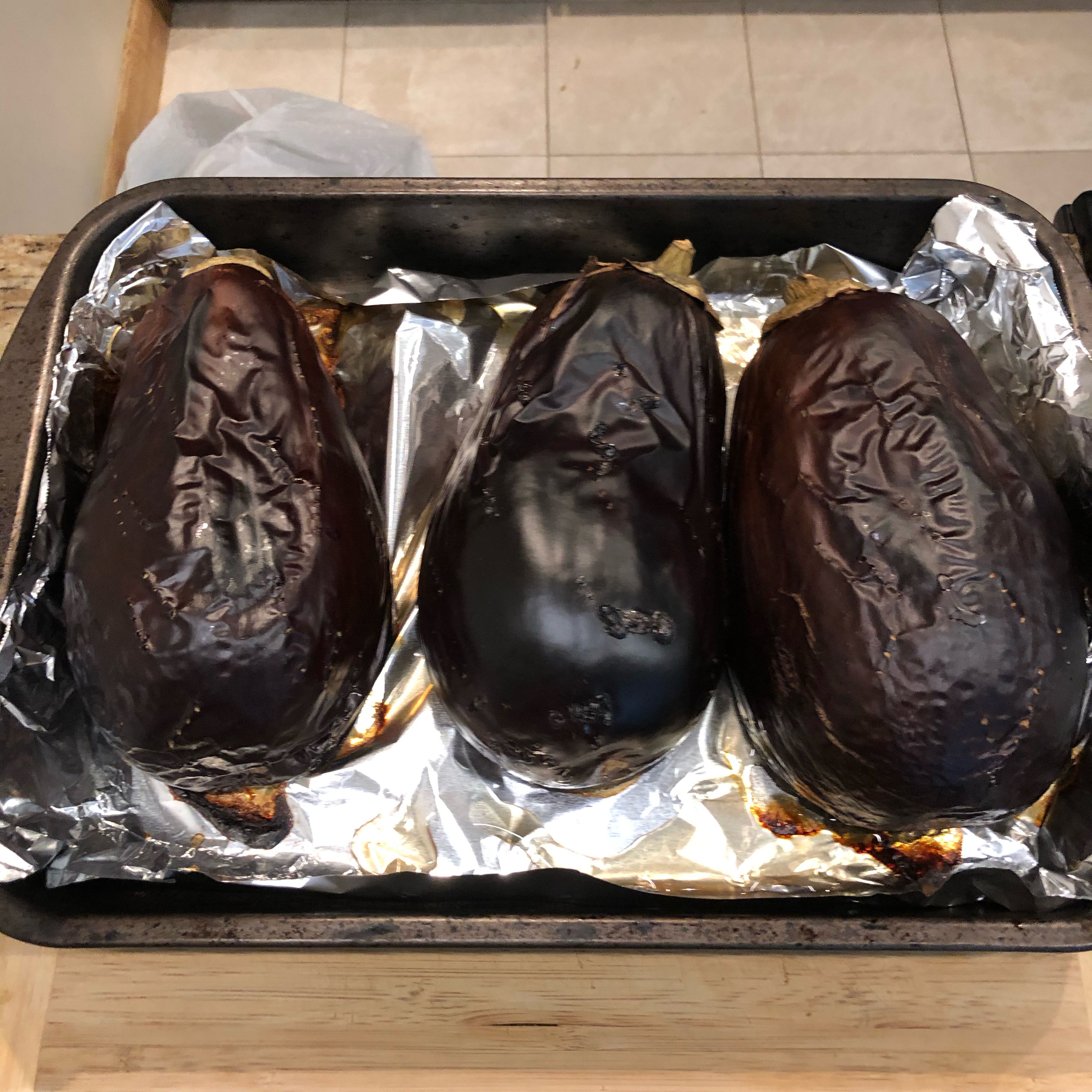 Put foil paper in a pan and place eggplants side by side. If you can make the stalk opposite direction of one another (optional). Broil on high for between 30mins to 45mins. It might be longer or shorter depending on your oven. You want to take the eggplants out of the oven once they are soft. (Pictured above)