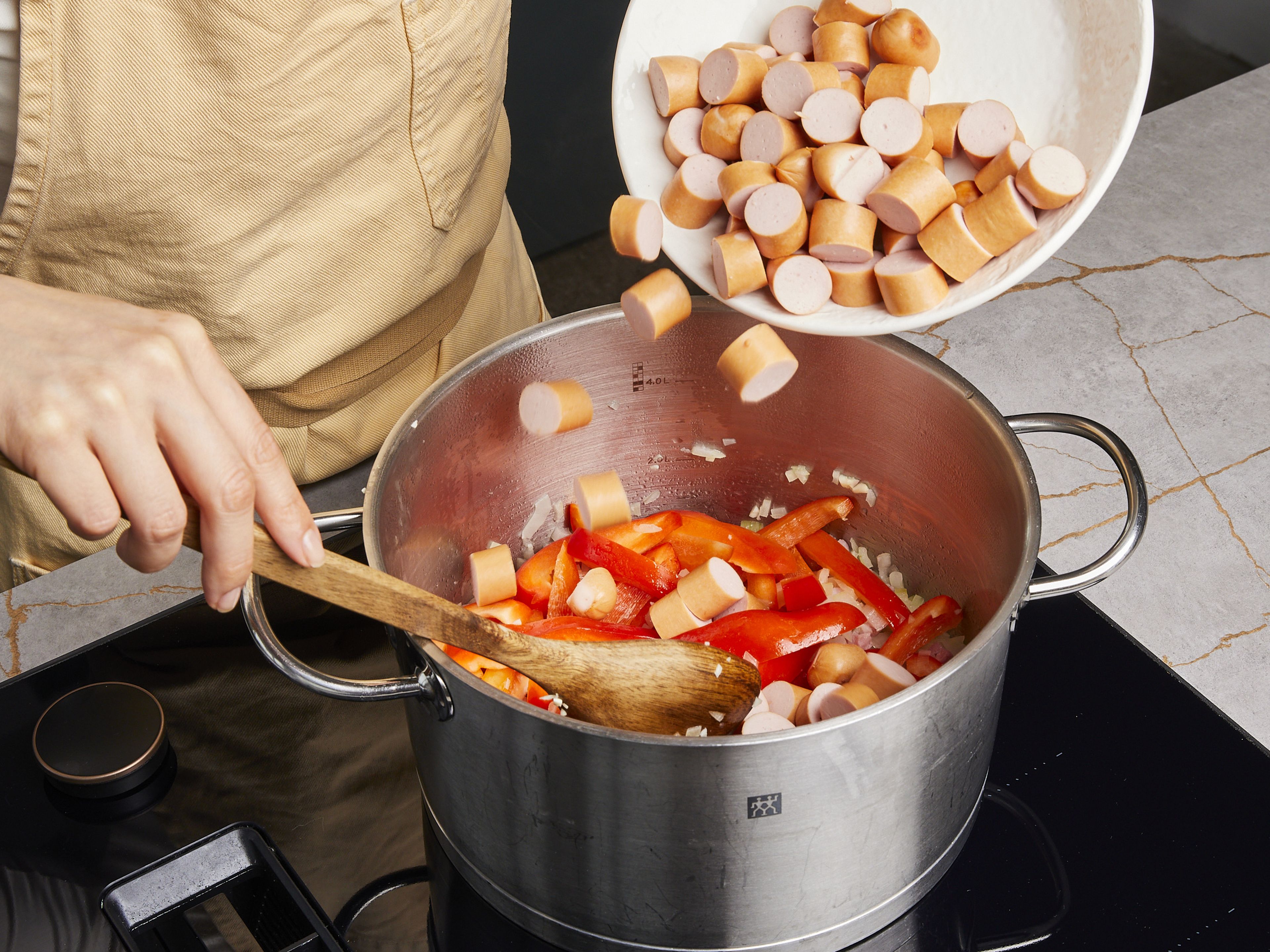 Heat some oil in a large pot, add bacon, onion, and garlic to sauté for approx. 1–2 min. Then, add bell peppers and sausages to fry for approx. 1–2 min. more. Add paprika powder and tomato paste and fry for a few more minutes.