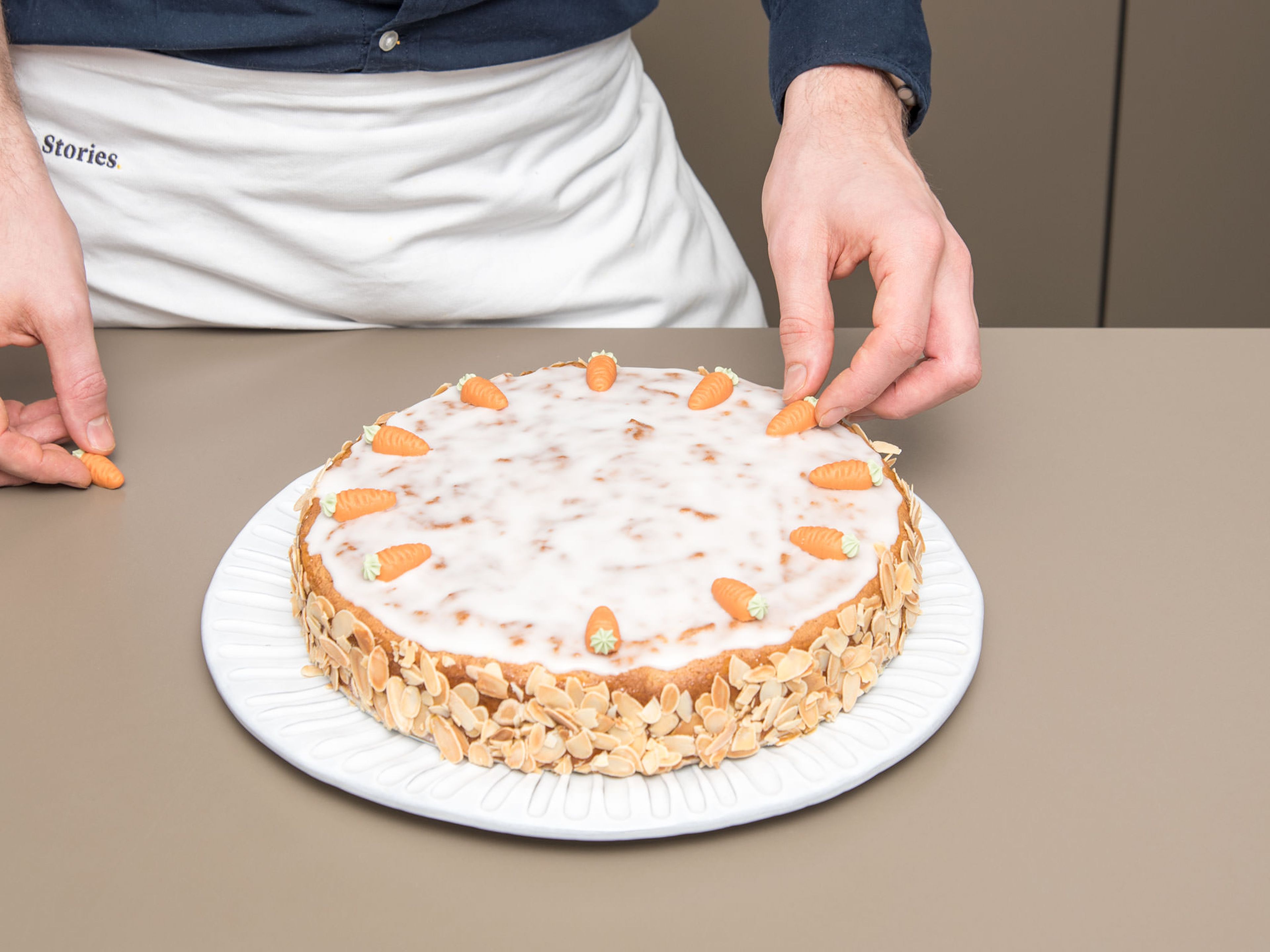 Sieve confectioner’s sugar into a small bowl, and add water to make a thick icing. With a palette knife coat cake with apricot jam and evenly brush with icing. Decorate sides with roasted almond slices and the top with marzipan carrots. Enjoy!