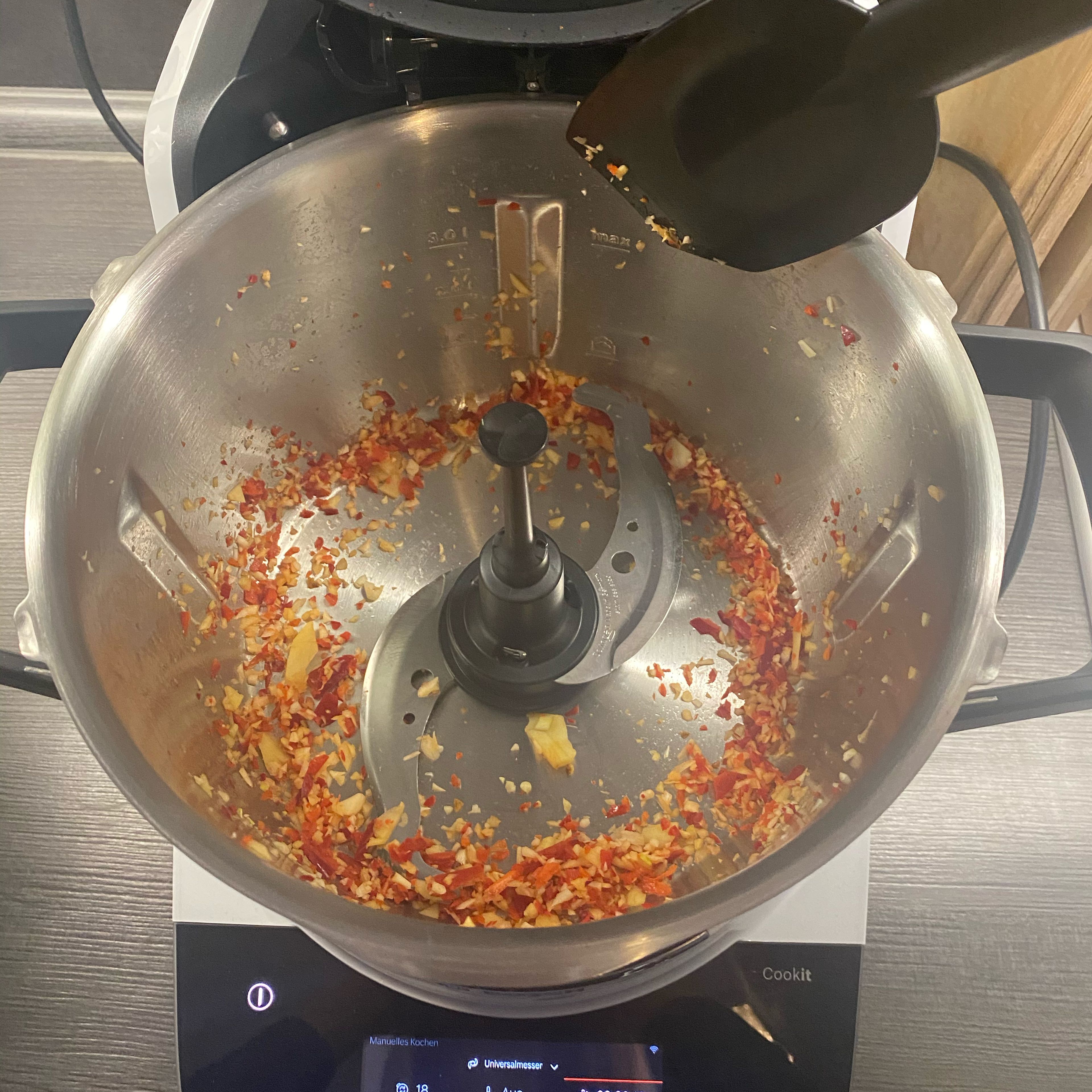 Universalmesser in den Cookit einsetzen. Chili entkernen und längs halbieren, Ingwer schälen und in Scheiben schneiden und zusammen mit den Knoblauchzehen in den Topf geben und bei geschlossenem Deckel zerkleinern (Universalmesser| Stufe 18 | 5 Sek.).