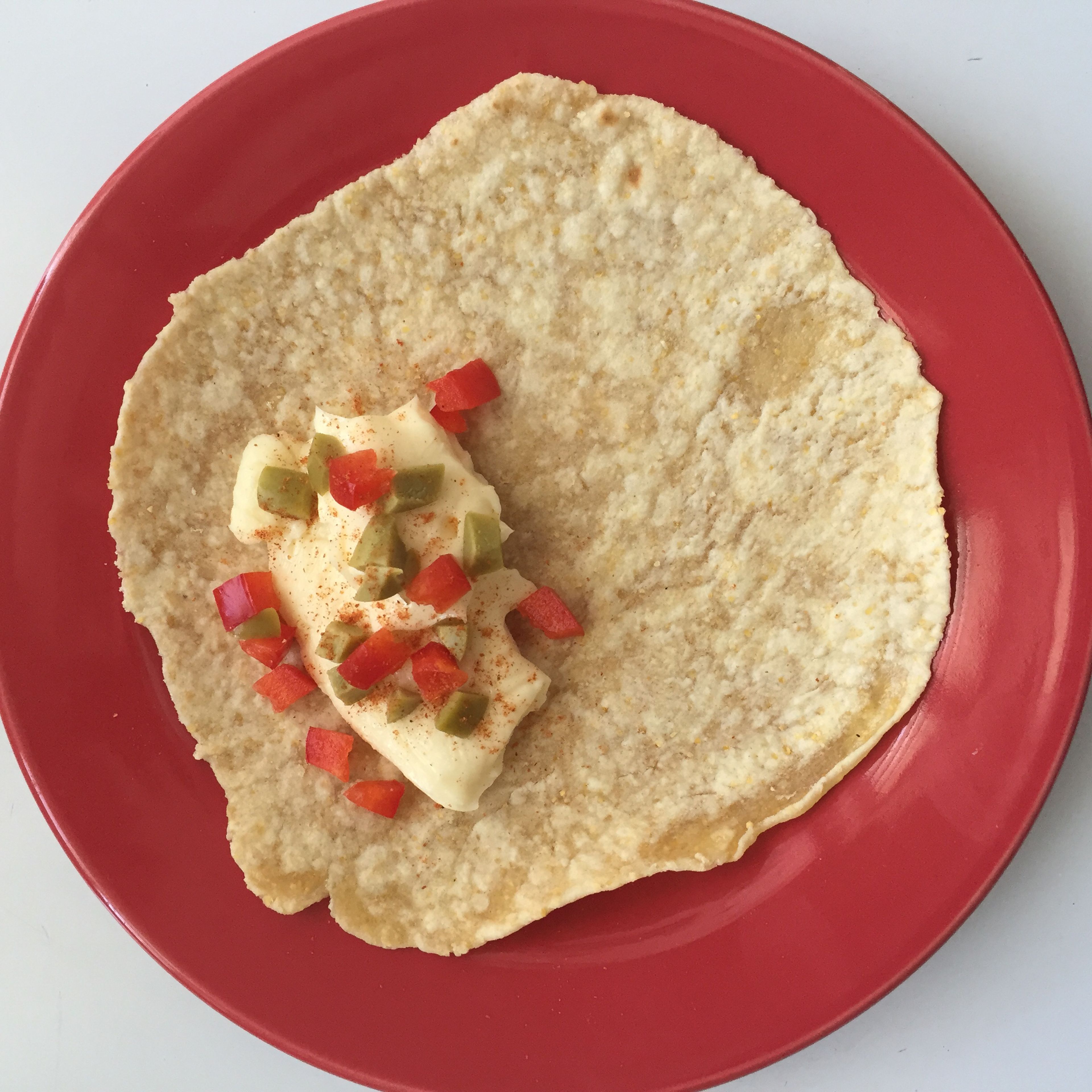 Place corn tortilla over a dish, and add loaf of cheese, diced red bell pepper, diced onions and cayenne pepper to taste.