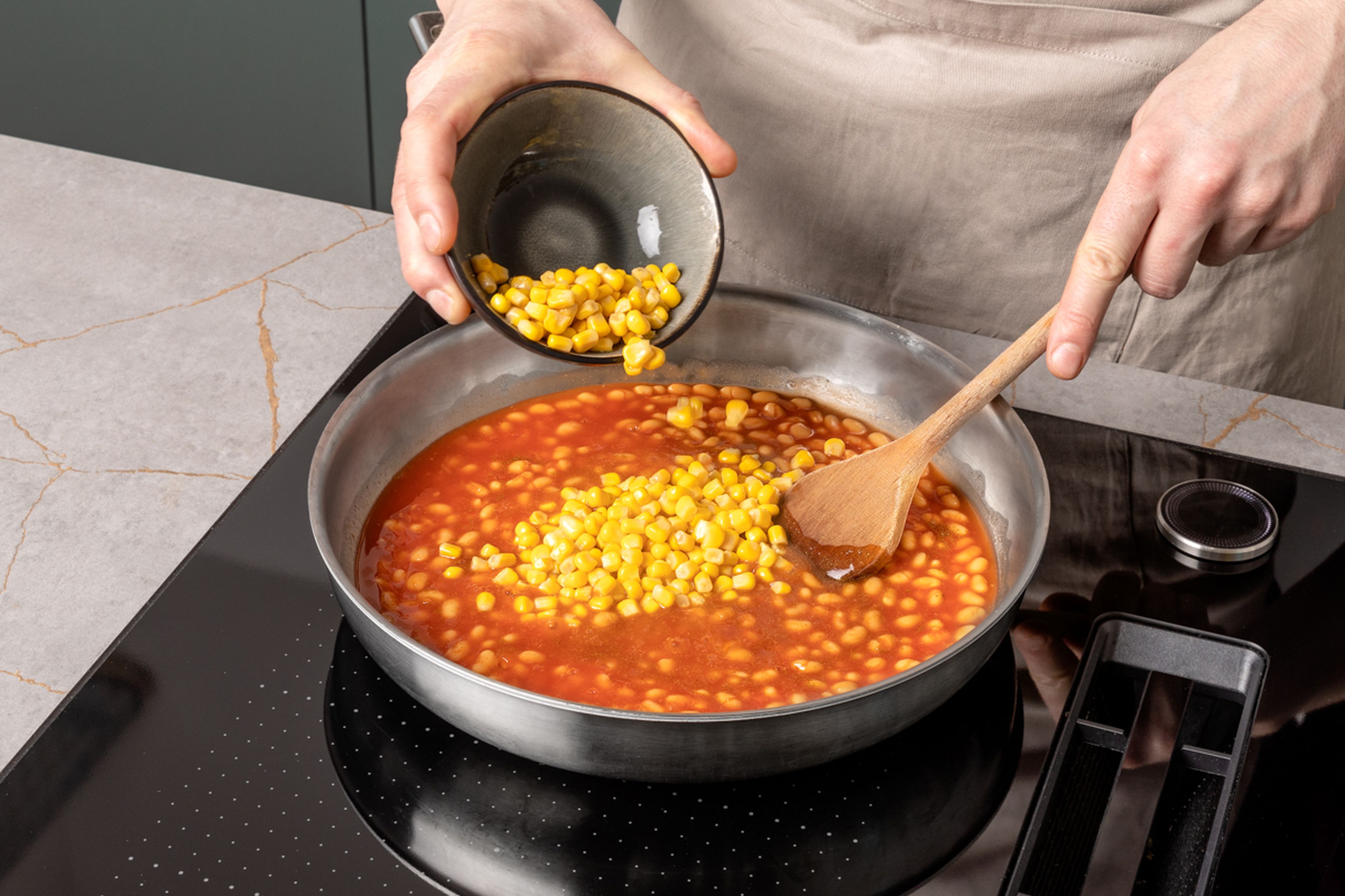 In the meantime, finely chop garlic. Heat oil in a large frying pan and sweat garlic in it for approx. 1 min. until translucent. Add baked beans, drained corn, and cumin and simmer together for approx. 2–3 min. Season to taste with salt and pepper.