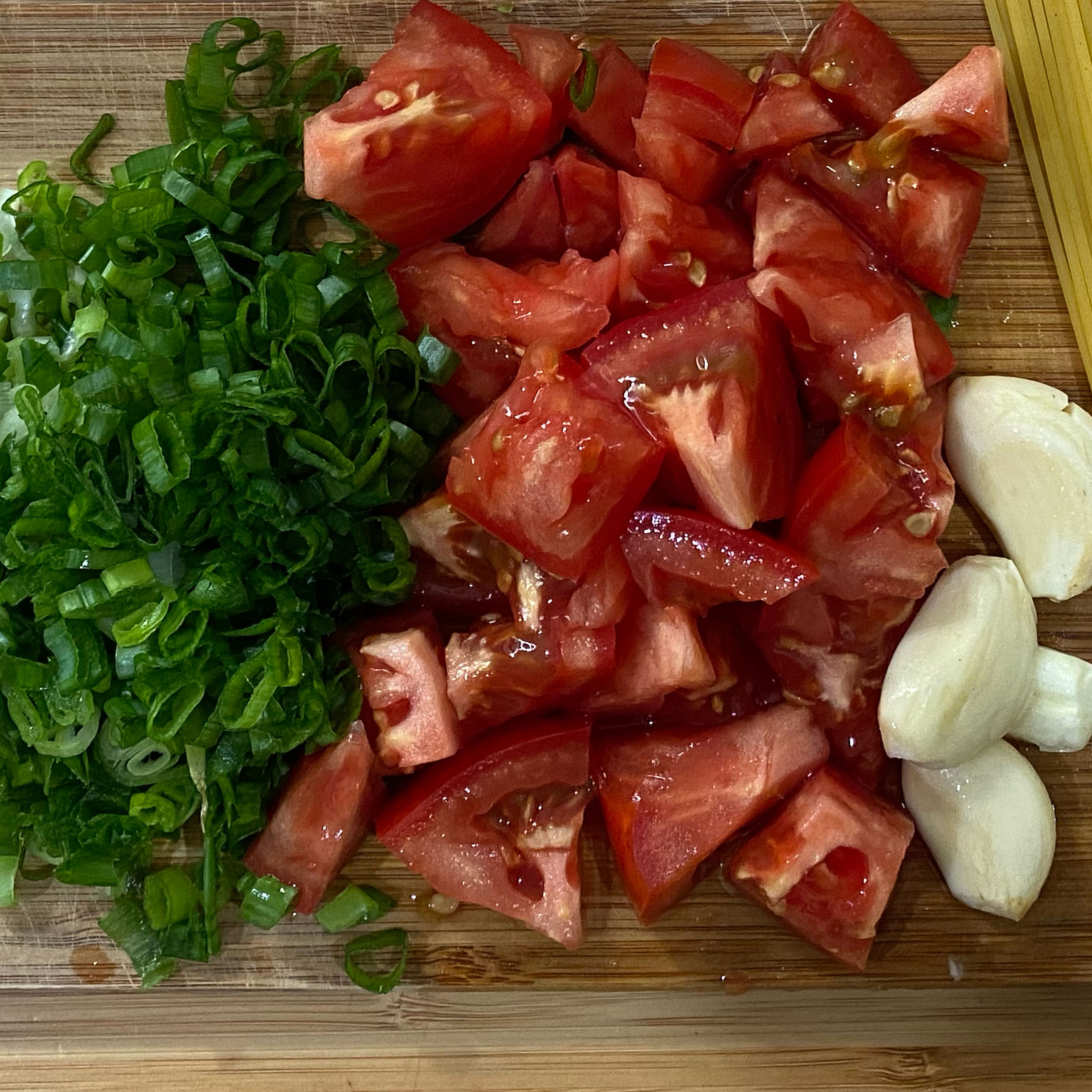 While spaghetti is boiling, chop tomatoes, slice green onions, and crush the garlic