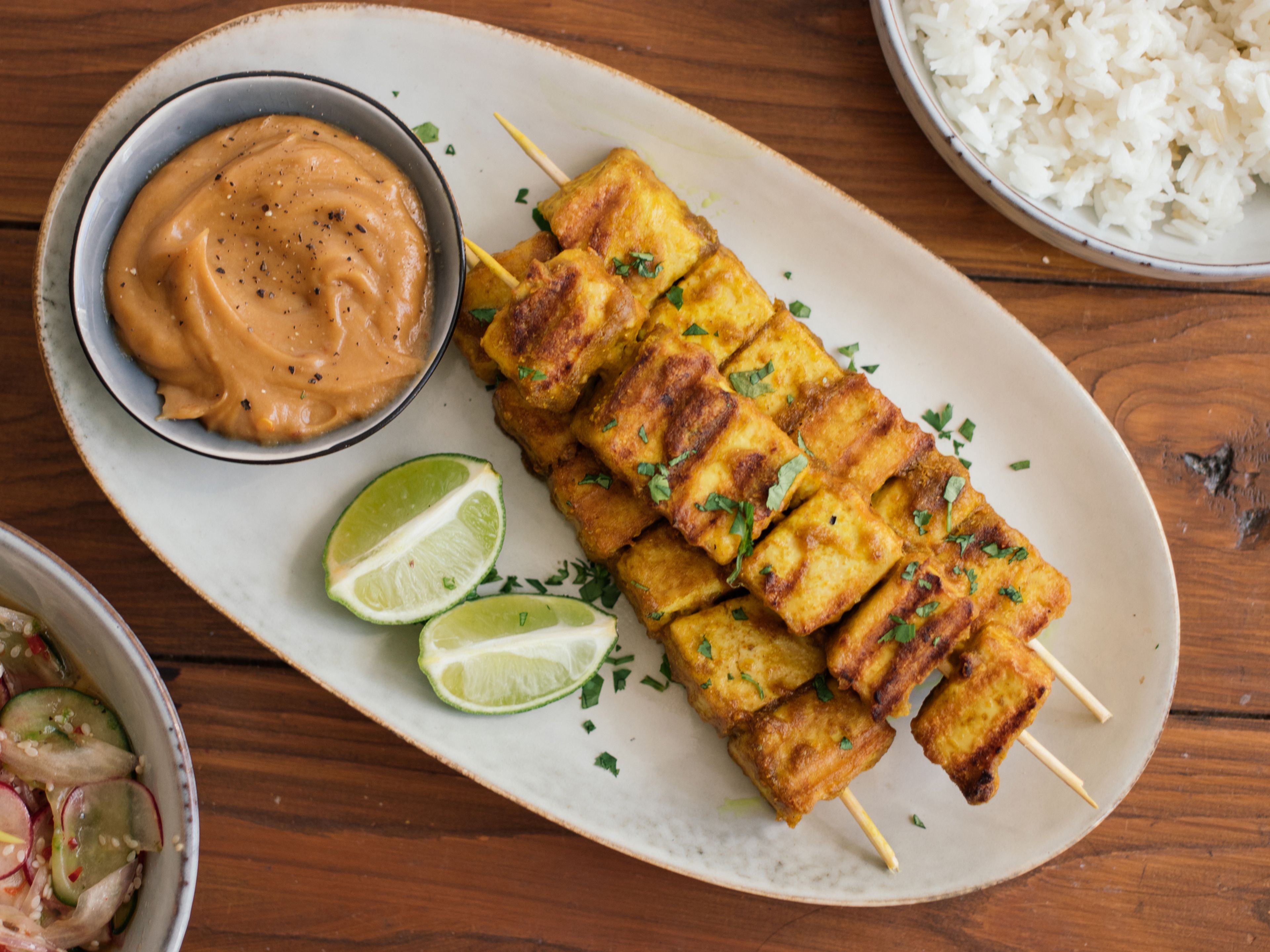 Serve tofu skewers with peanut dip, cucumber and radish salad, and cooked rice. Sprinkle with chopped cilantro and sesame seeds. Enjoy!