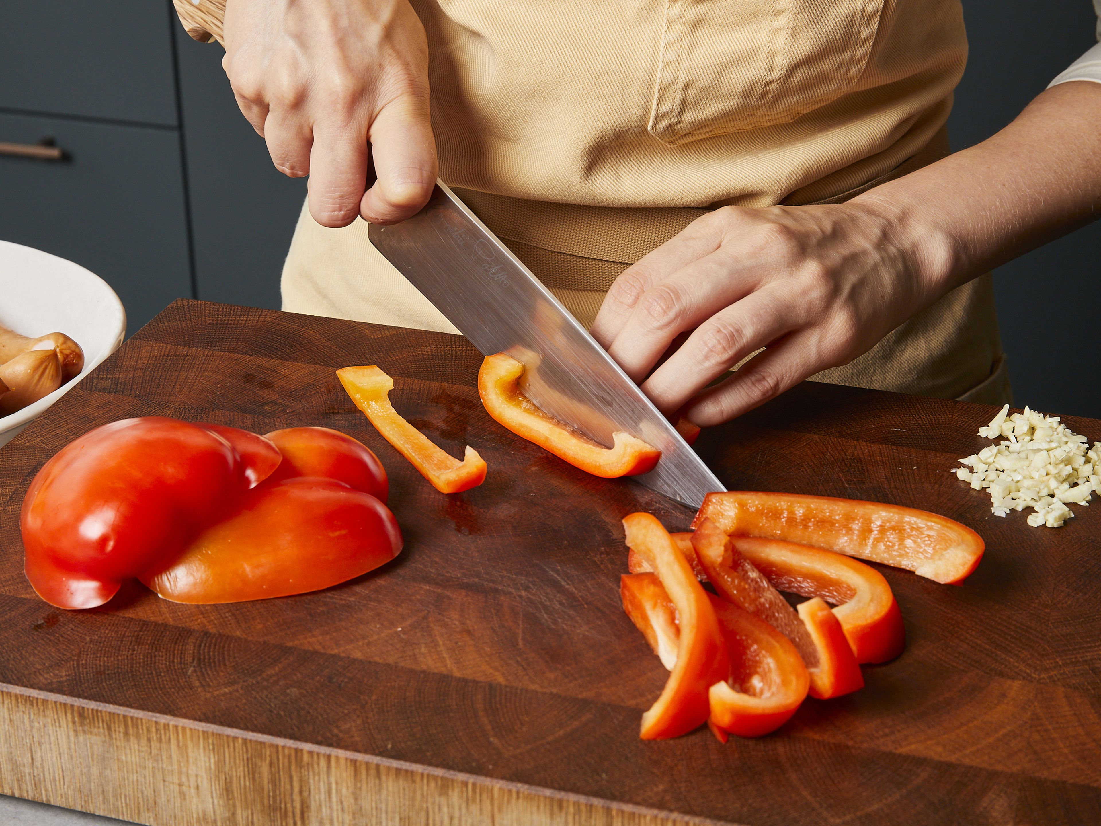 Peel onion and garlic, dicing the onion and finely chopping the garlic. Remove the core from bell peppers and cut into strips. Cut sausages into bite-sized pieces.