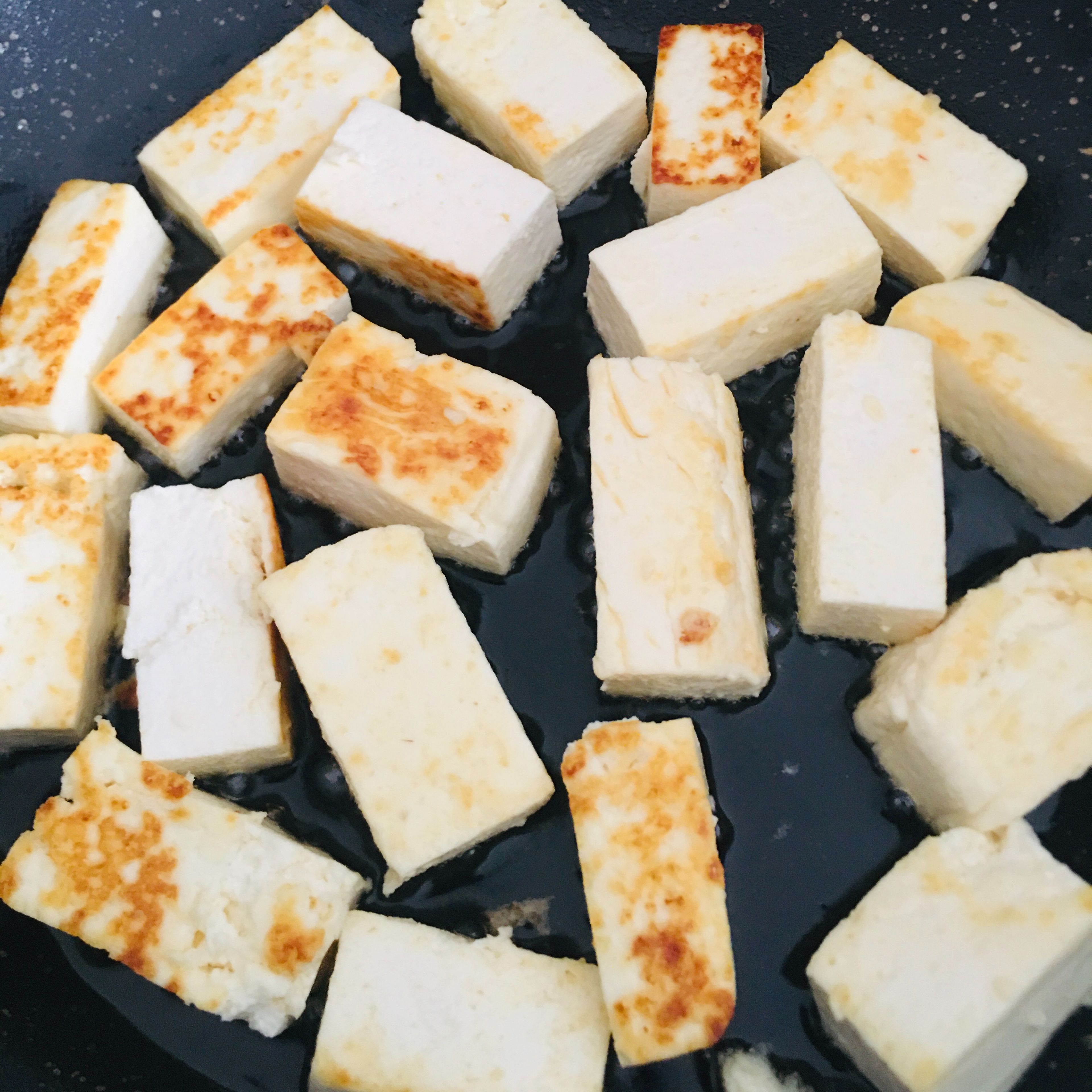While the gravy is getting ready, go ahead and fry the indian cottage cheese (paneer) cubes. Start with by heating the second pan with a bit of oil in it. Once the oil is hot, place the paneer cubes and let it turn golden brown on one side before flipping it. It is necessary to use a non-stick pan as paneer tends to stick to the bottom. Be gentle while flipping them as they are soft and tender at this stage.