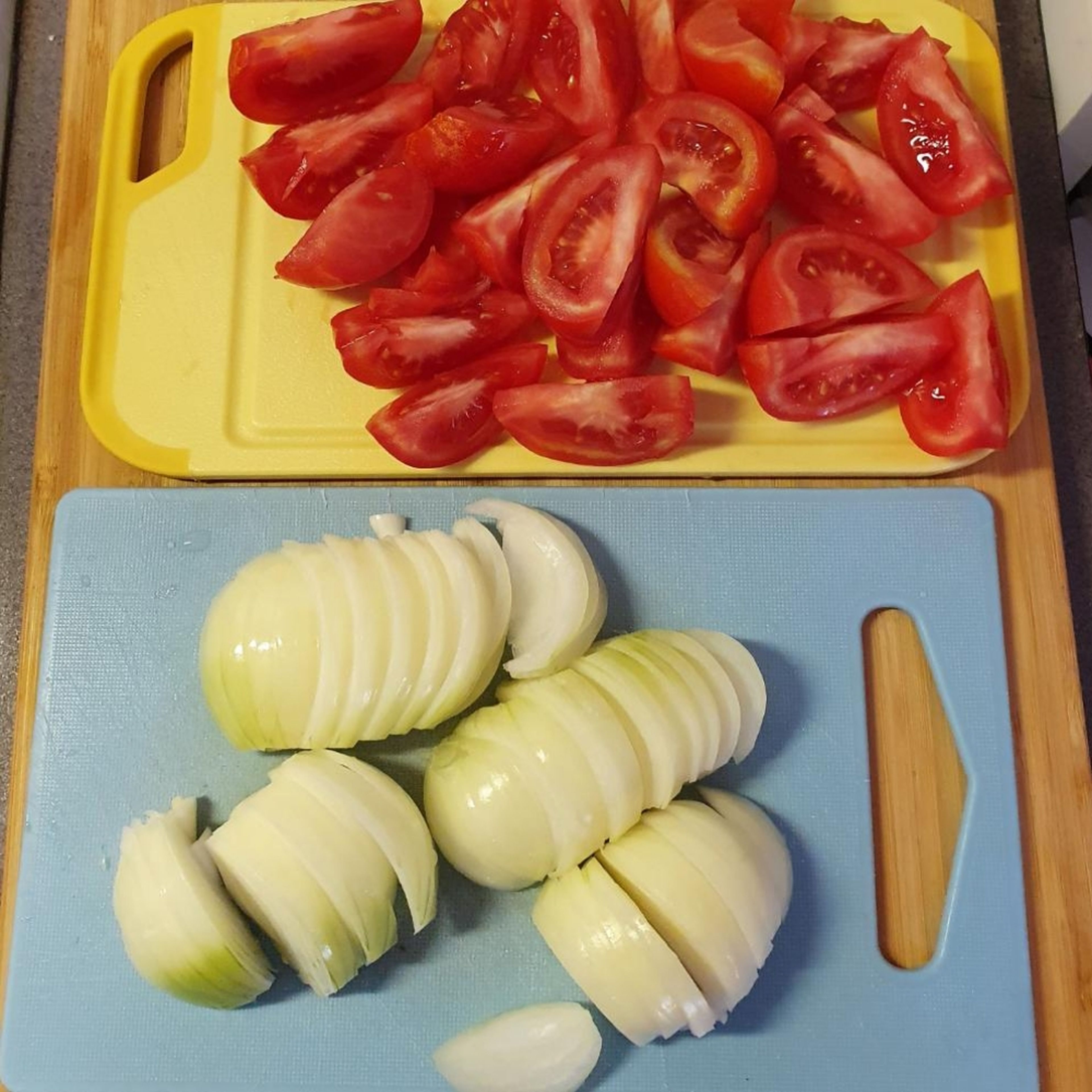 In der Zwischenzeit Zwiebeln abziehen und in Streifen schneiden, von den Tomaten den grünen Strunk entfernen und in 6 Stücke schneiden.