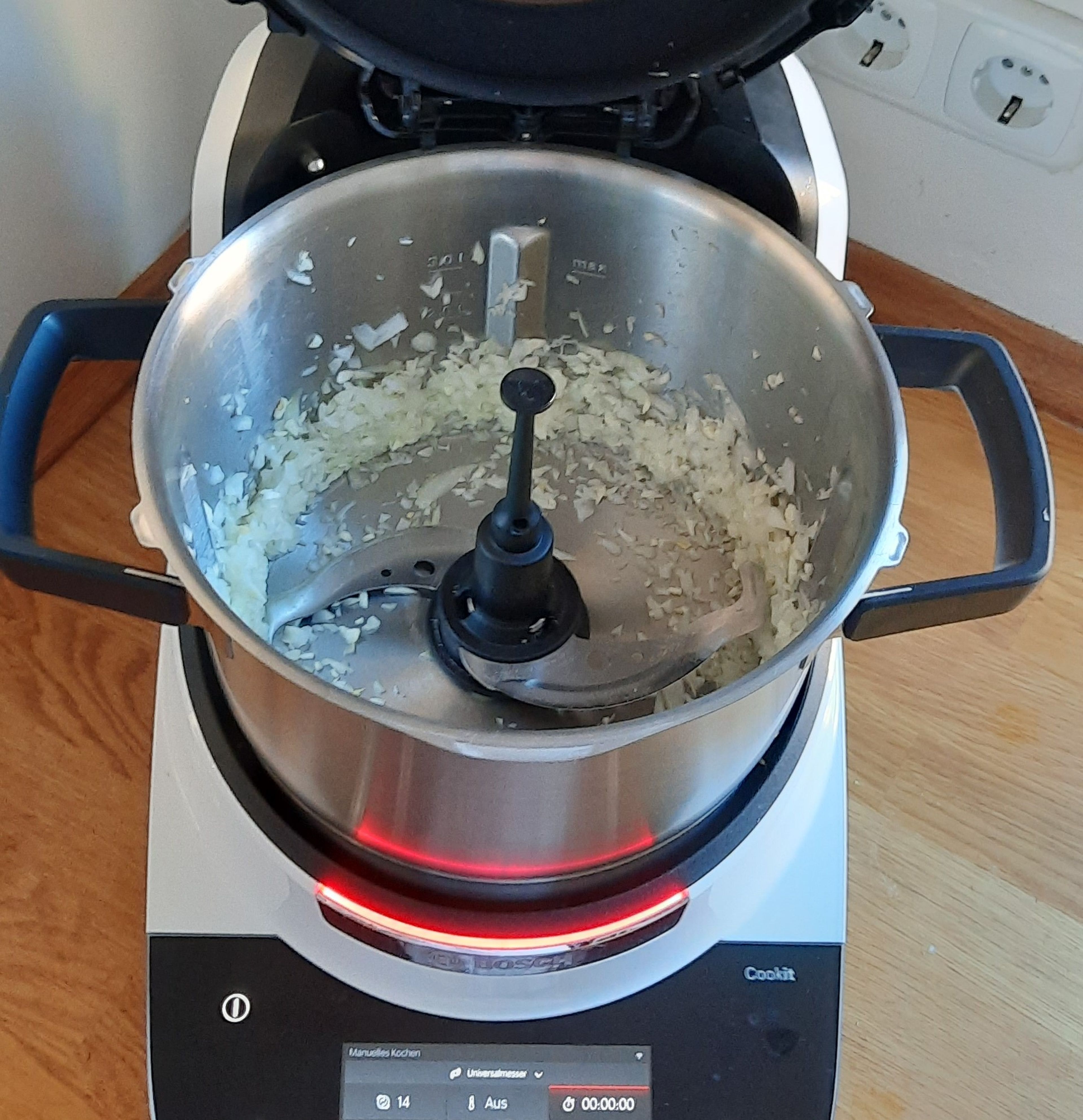 Das Gemüse vom Dampfgaraufsatz herunternehmen und zur Seite stellen. Cookit einmal ausleeren und das Universalmesser einsetzen. Die Zwiebel schälen und vierteln und die beiden Knoblauchzehen schälen. Alles in den Topf geben und den Deckel schließen. Den Messbecher einsetzen und zerkleinern (Universalmesser I Stufe 14 I 10 Sek.).