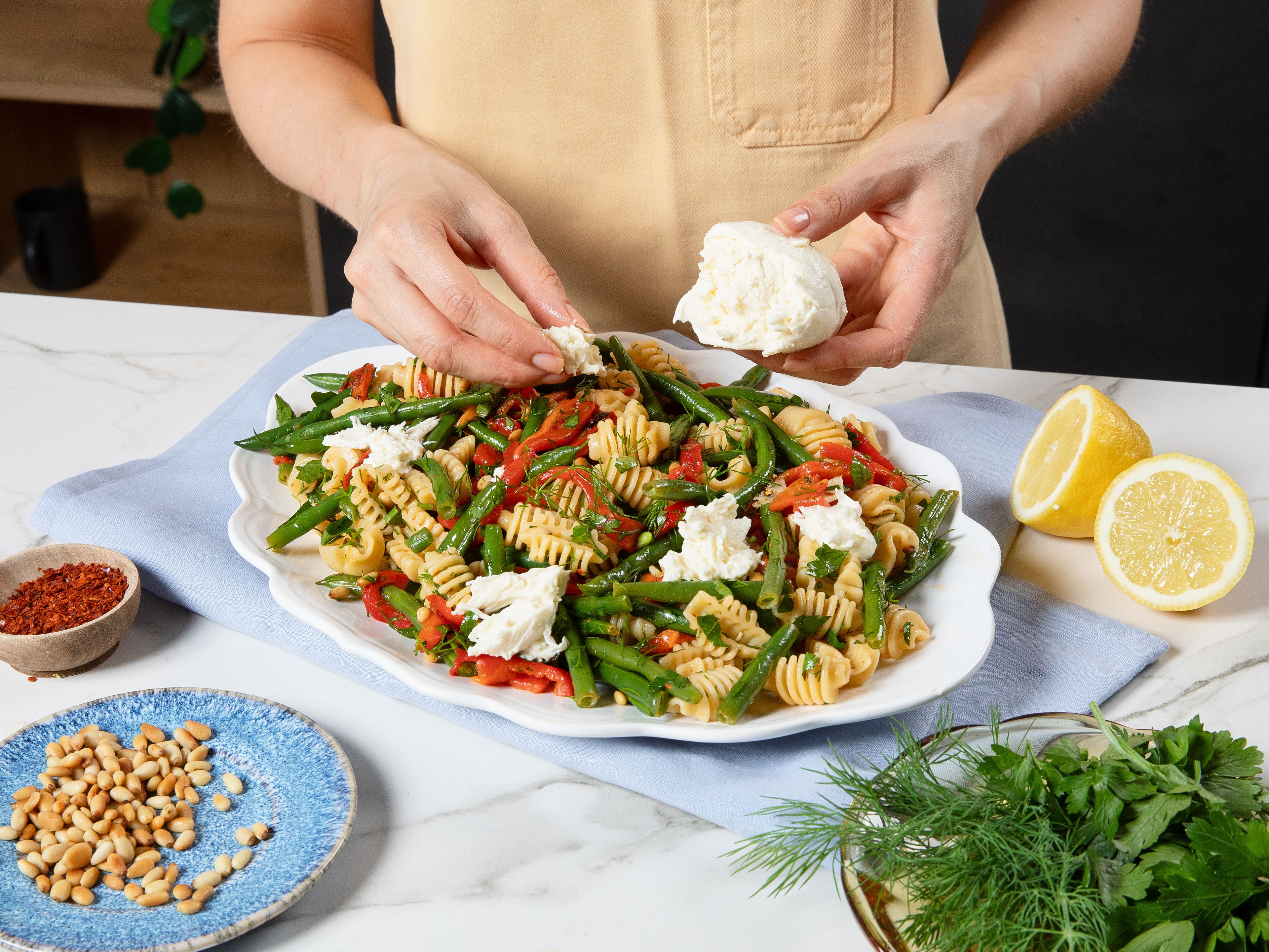 Die Petersilie und den Dill grob hacken und zusammen mit den gerösteten Pinienkernen, Zitronensaft und Balsamicoessig zur Pasta geben. Alles vorsichtig vermengen und großzügig mit Salz und Pfeffer abschmecken. Auf einer Servierplatte anrichten, den Mozzarella in Stücke zupfen und kurz vor dem Servieren über den Salat geben. Mit Chiliflocken, etwas Zitronenabrieb und weiteren Kräutern garnieren und lauwarm servieren.