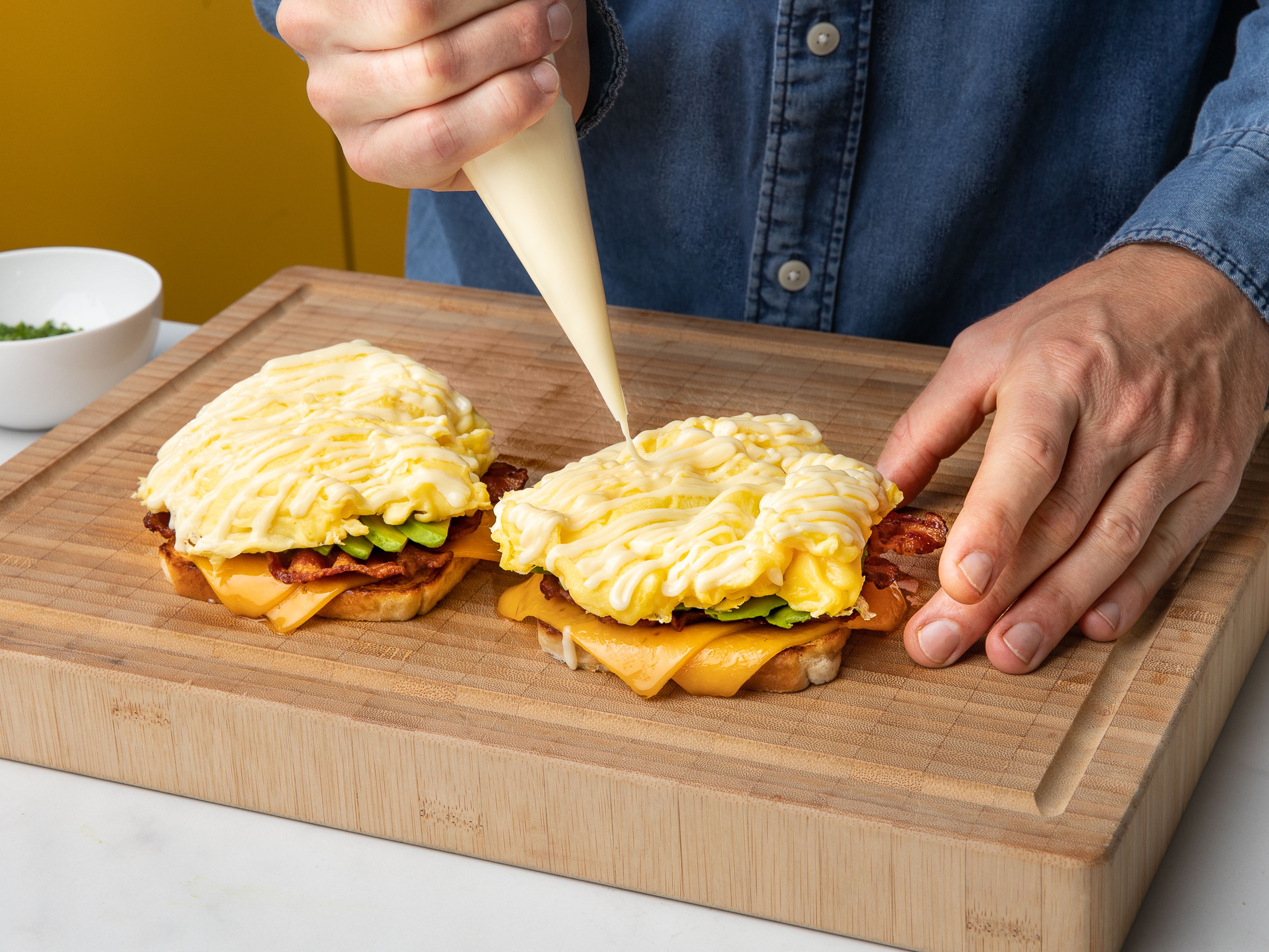 Zum Zusammensetzen des Sandwiches zunächst eine Scheibe Speck, dann ½ Avocado und schließlich das Ei auf die Toasts mit Käse geben. Mayonnaise darübergeben, mit dem Schnittlauch bestreuen und mit einer Scheibe Toast toppen.