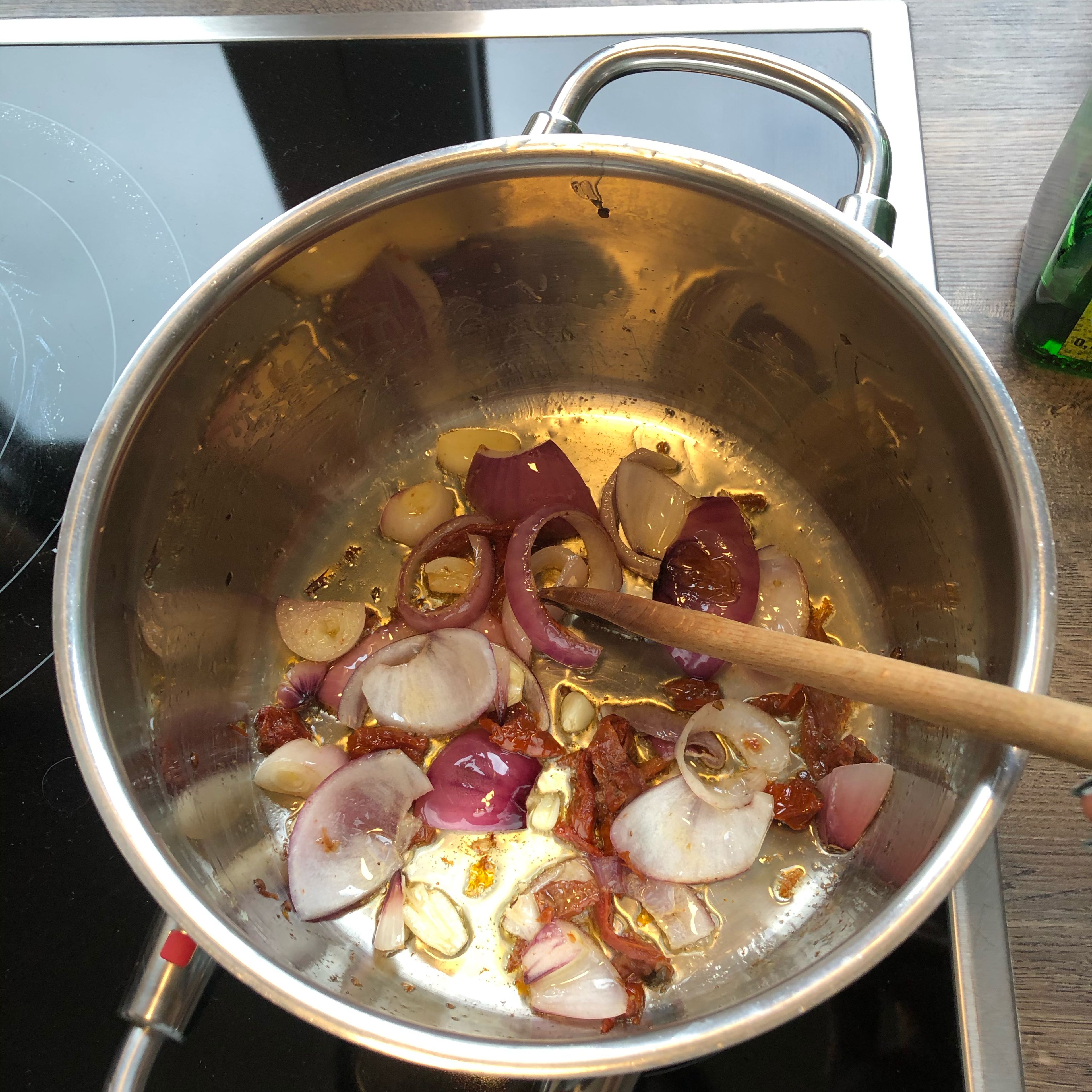 Einen Topf aufstellen und etwas Öl hinzugeben (erst wenn der Topf heiß ist). In der Zwischenzeit Knoblauch und Zwiebeln schneiden. Und in den Topf geben, kurz anbraten und dann die getrockneten Tomaten hinzugeben.
