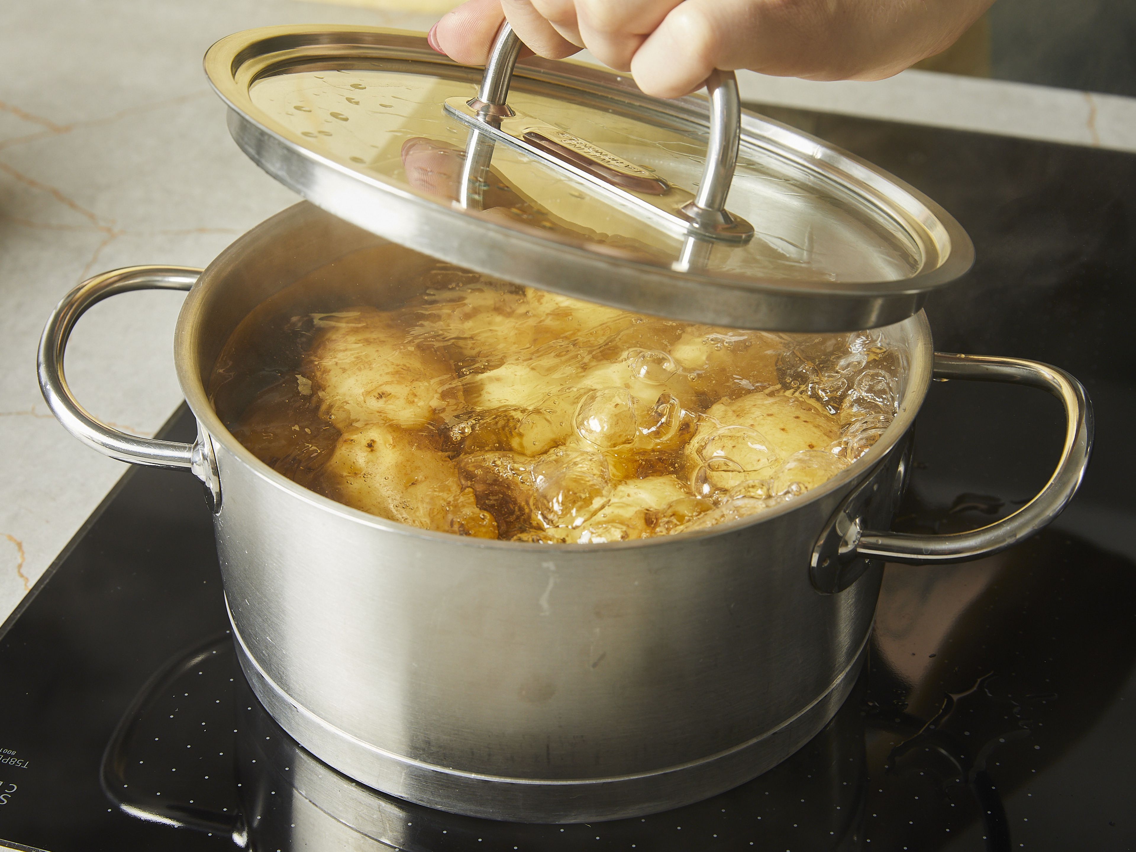 Den Backofen auf 220°C Ober-/Unterhitze (200°C Umluft) vorheizen. Ganze Kartoffeln mit Schale in einen großen Topf geben und mit kaltem Wasser bedecken. Zum Kochen bringen und ca. 30 Min. kochen oder bis die Schale leicht aufplatzt und die Kartoffeln weich genug sind, um sie mit einem Messer einstechen zu können. Das Wasser abgießen und Kartoffeln auf ein Abkühlgitter legen und mindestens ca. 5 Min. ausdampfen lassen. Dann die Kartoffeln in einen großen Bräter oder eine Auflaufform geben (Gusseisen ist ideal, aber Glas oder Metall eignen sich auch. Keramik sollte vermieden werden.).