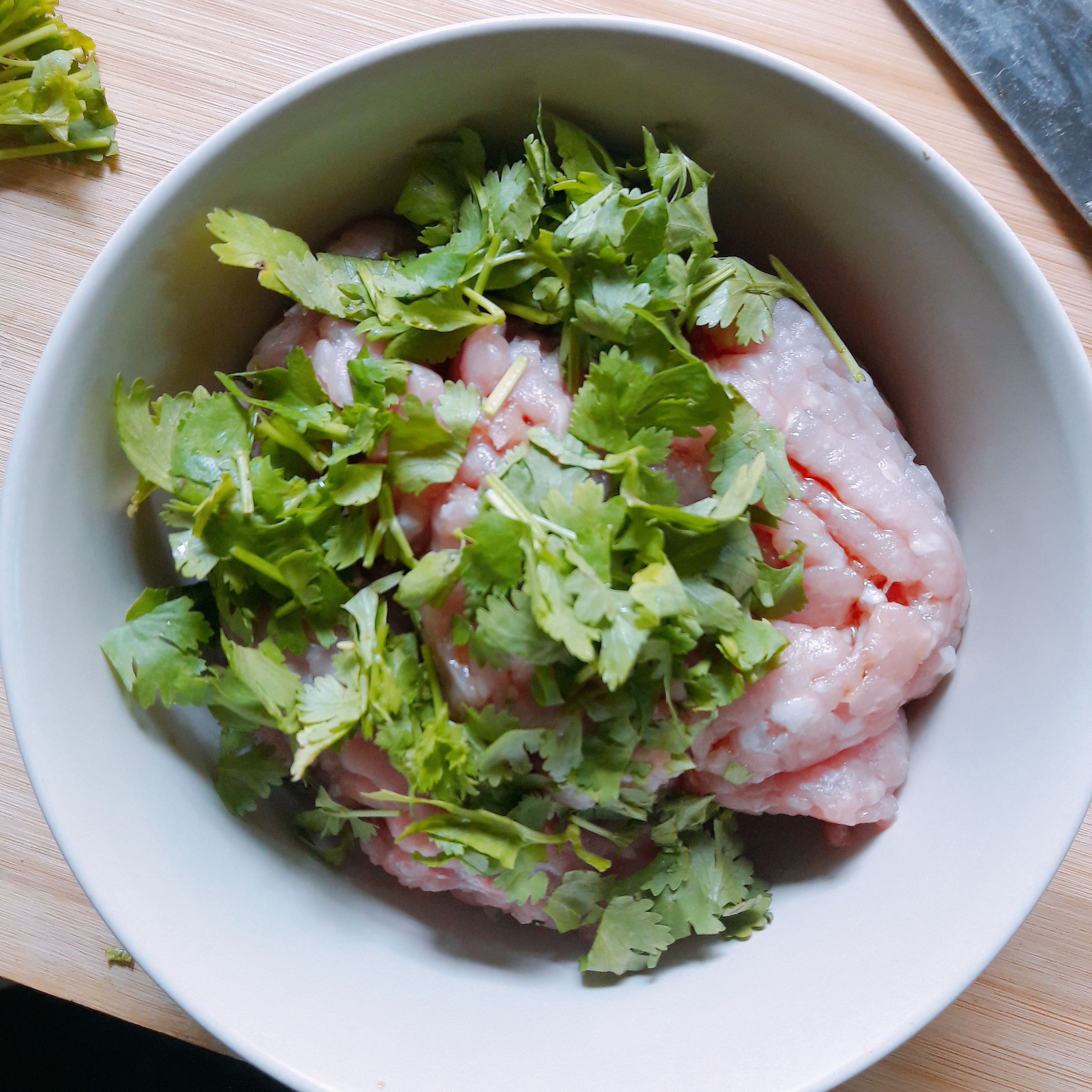 To make the dumplings filling, take the bacon and chop into small pieces and place in the pork bowl. Then add some coriander leaves, salt, pepper, soy sauce and an egg. Use chopsticks or a fork to vigorously mix the filling until the texture becomes very sticky.