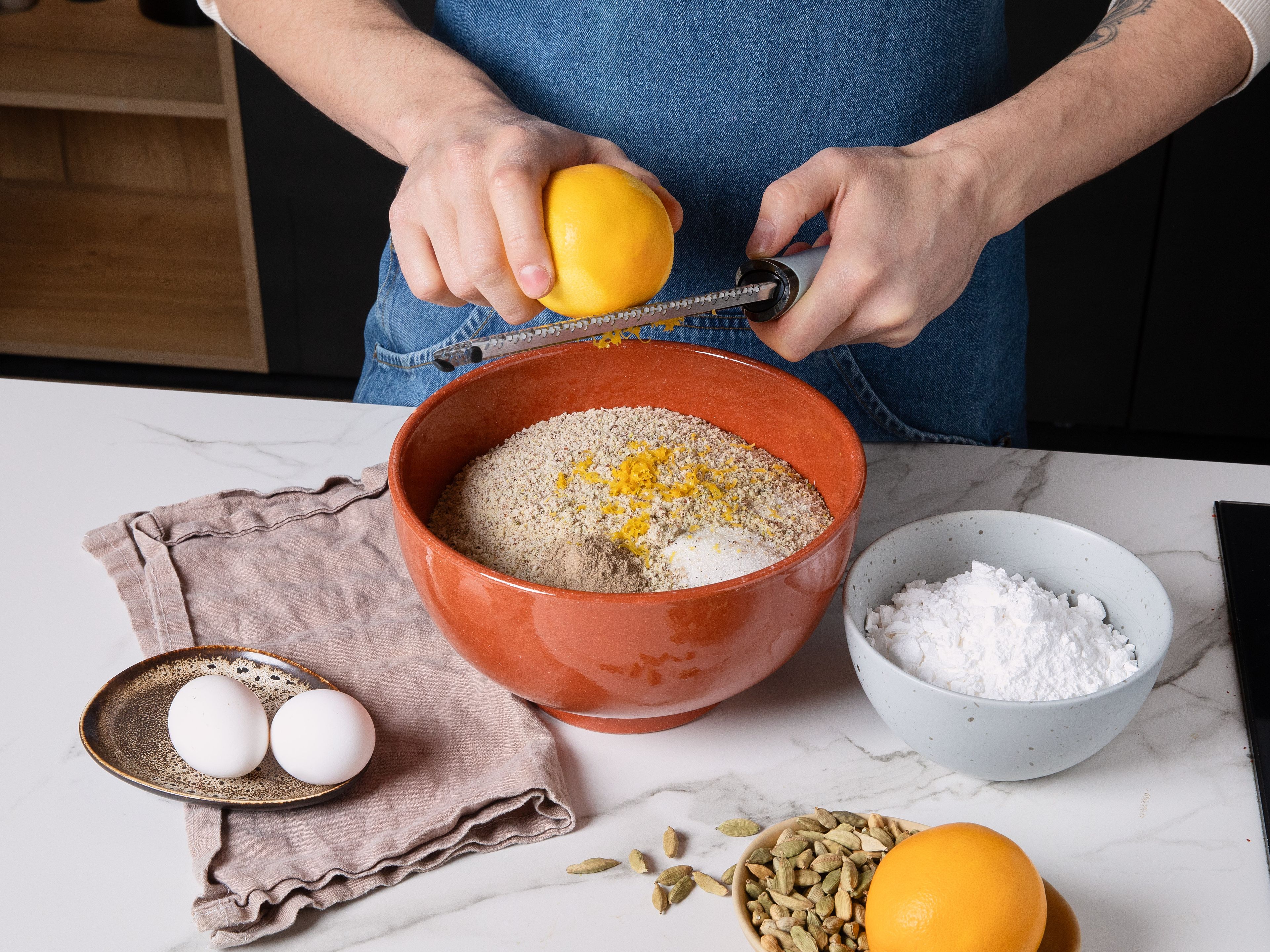 Preheat oven to 120°C/248°F on convection. Finely zest orange. Then, place pistachios in a food processor and finely grind them with ground almonds, orange zest, powdered sugar, ground cardamom, and a pinch of salt. Transfer to a bowl, add egg whites and vanilla sugar, then knead everything into a pliable dough. Wrap it in plastic wrap and let it rest in refrigerator for approx. 30 min.
