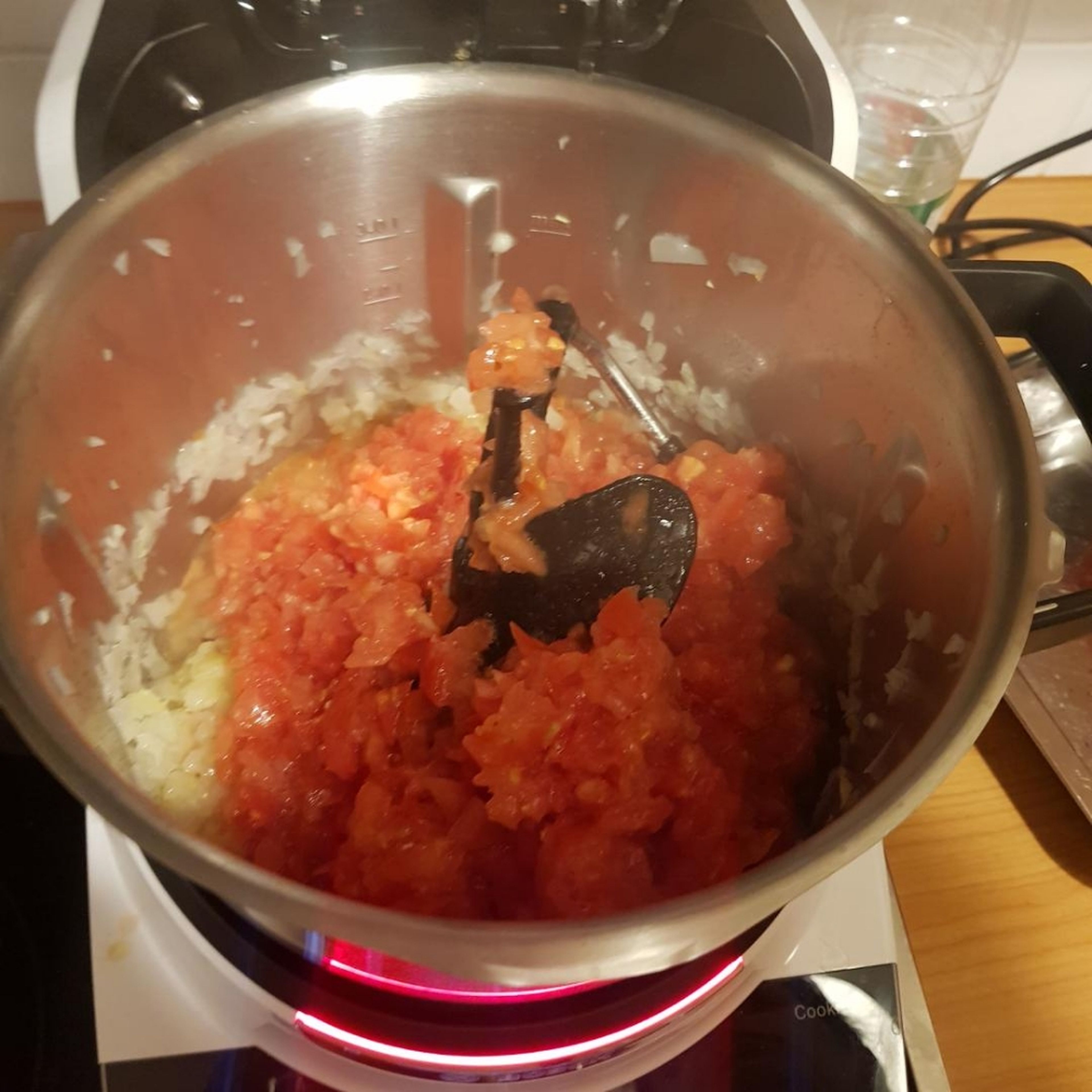 Deckel öffnen und die vorher zerkleinerten Tomaten und frische Chili, die getrocknete Chili, das Tomatenmark, Salz und Pfeffer hineingeben. Das Wasser einwiegen und den Deckel schließen (ohne Messbecher). Alle Zutaten im Topf anrösten (3-D Rührer | Stufe 5 | 200°C | 8 min).