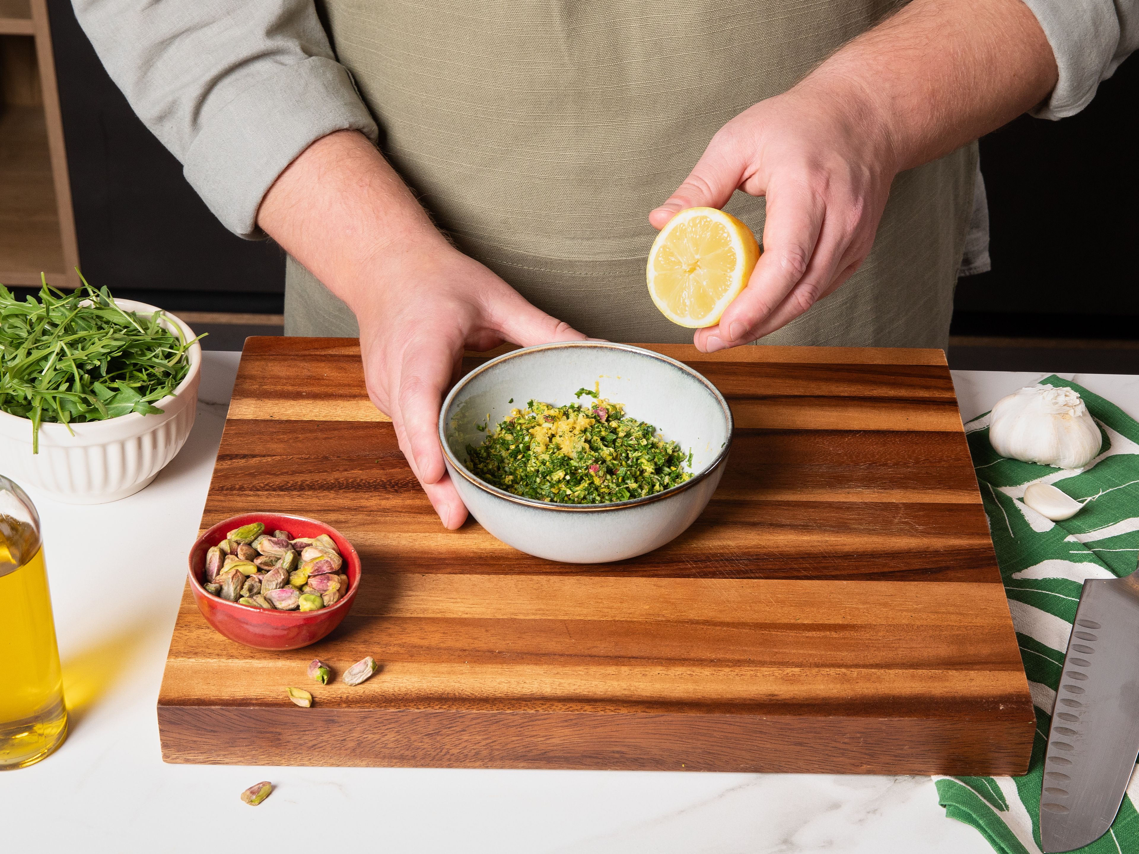 Für die Gremolata Knoblauchzehen schälen und fein hacken. Etwas Rucola zum Garnieren beiseite legen und den Rest zusammen mit den Pistazien sehr fein hacken, dann alles in eine Schüssel geben. Die Hälfte des Knoblauchs hinzugeben, die Zitrone abreiben und die Zeste dazugeben sowie Zitronensaft. Mit der Hälfte des Olivenöls vermengen und mit Salz und Pfeffer abschmecken.