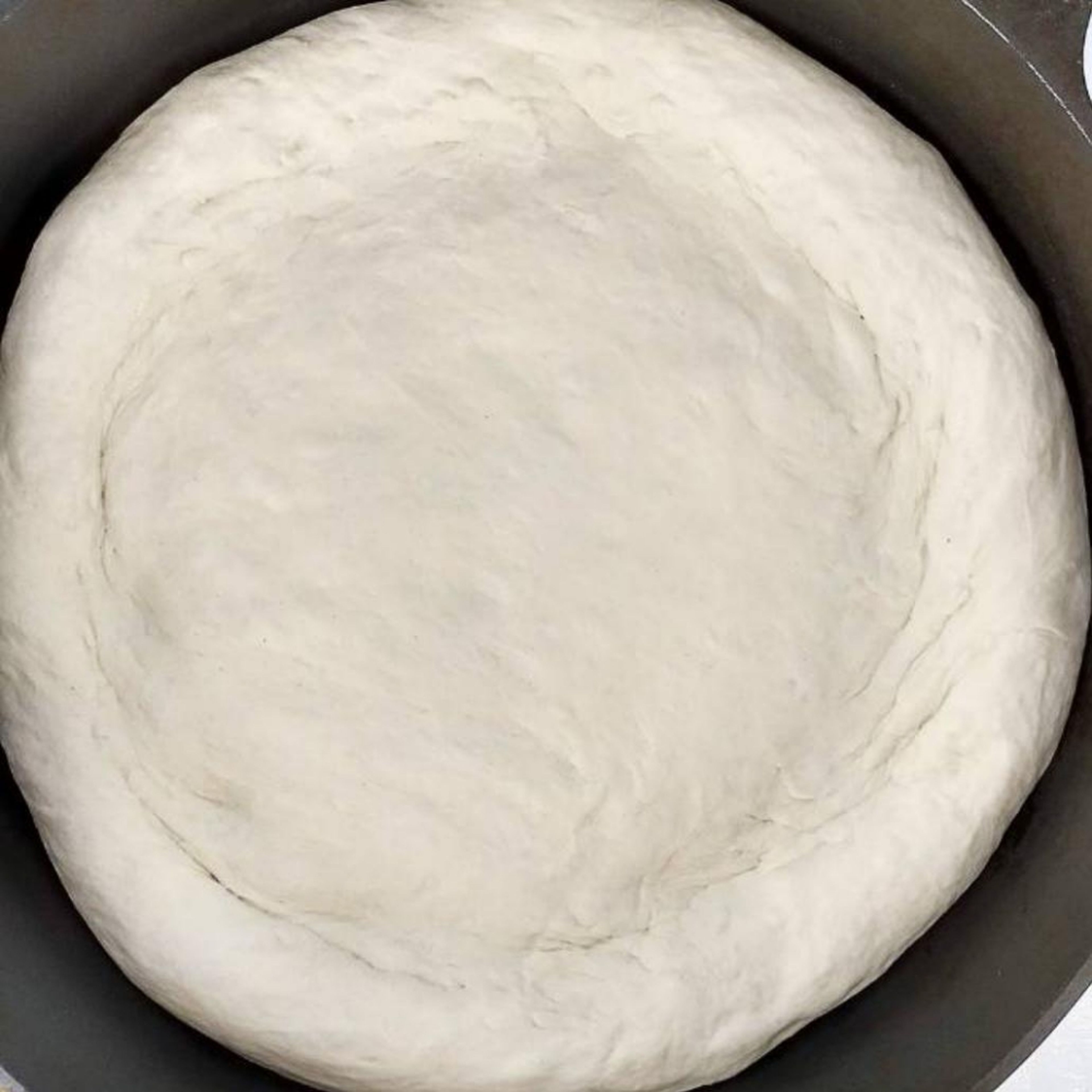 After an hour, put the dough on the table and create pats from it. Start heating the pan and put some olive oil in it. Put the dough pat in the pan and fit the dough to the size of the pan. Put the cover onthe pan and fry the dough on the small heat for 5min.
