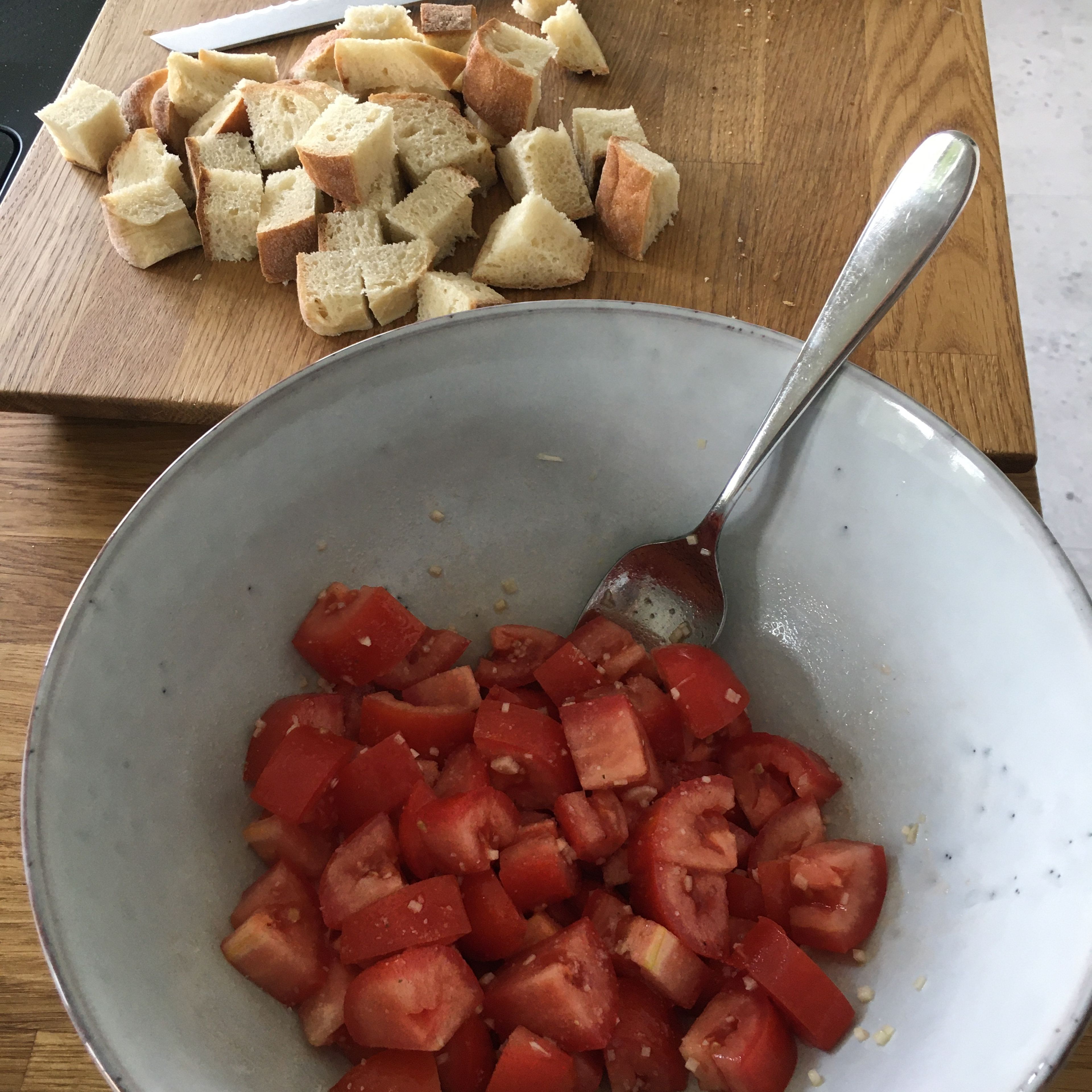 Brot in große Würfel schneiden. Tomate ebenfalls würfeln und mit fein gehacktem Knoblauch, Zucker, Salz und einem EL Olivenöl marinieren. Pinienkerne ohne Öl in der Pfanne rösten.
