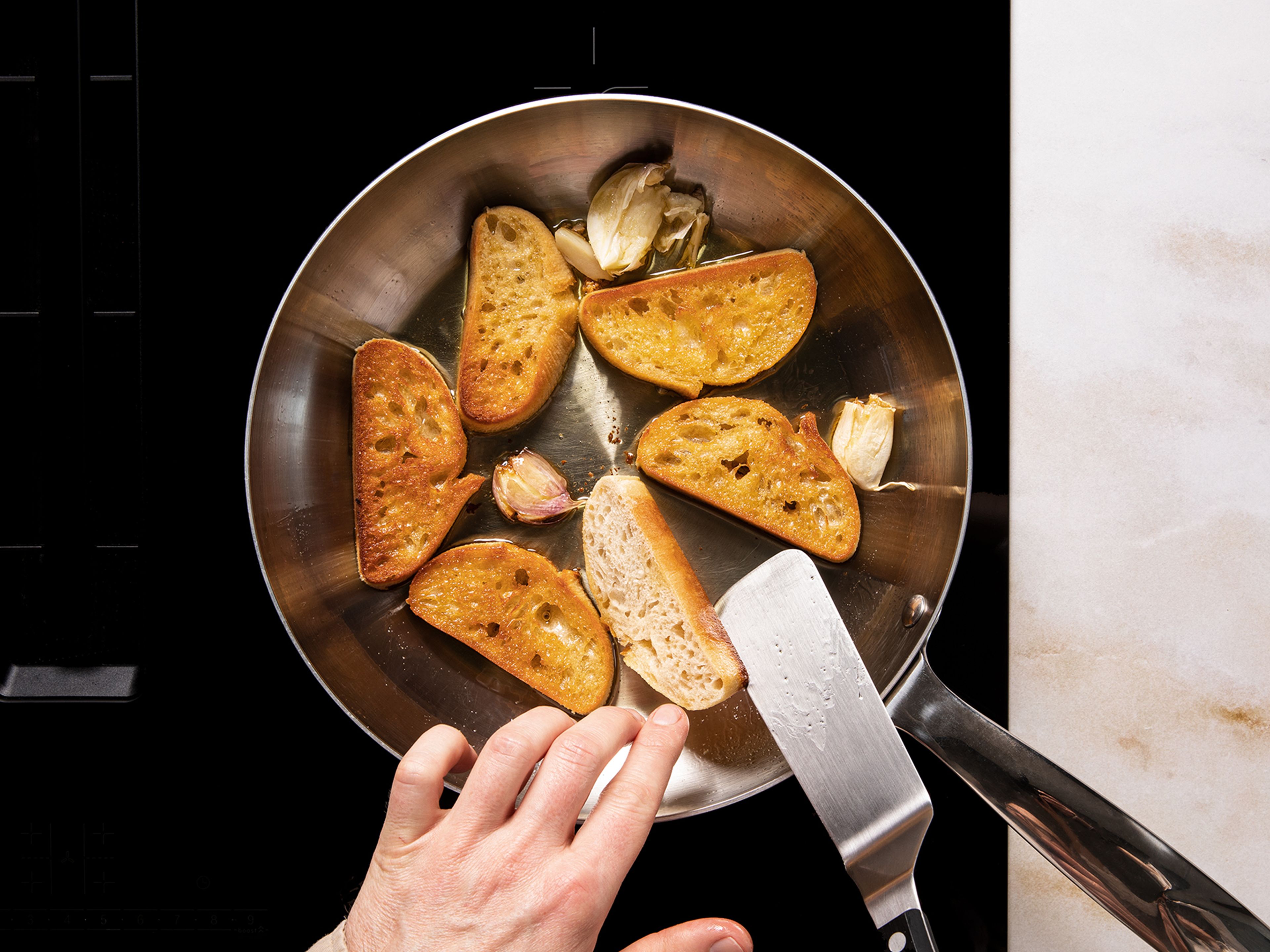 Das Ciabatta diagonal in 2 cm dicke Scheiben schneiden. Olivenöl bei mittlerer Hitze in einer Pfanne erhitzen und das Ciabatta von beiden Seiten gold-gelb anbraten. Das geröstete Brot mit einer Knoblauchzehe einreiben und salzen.