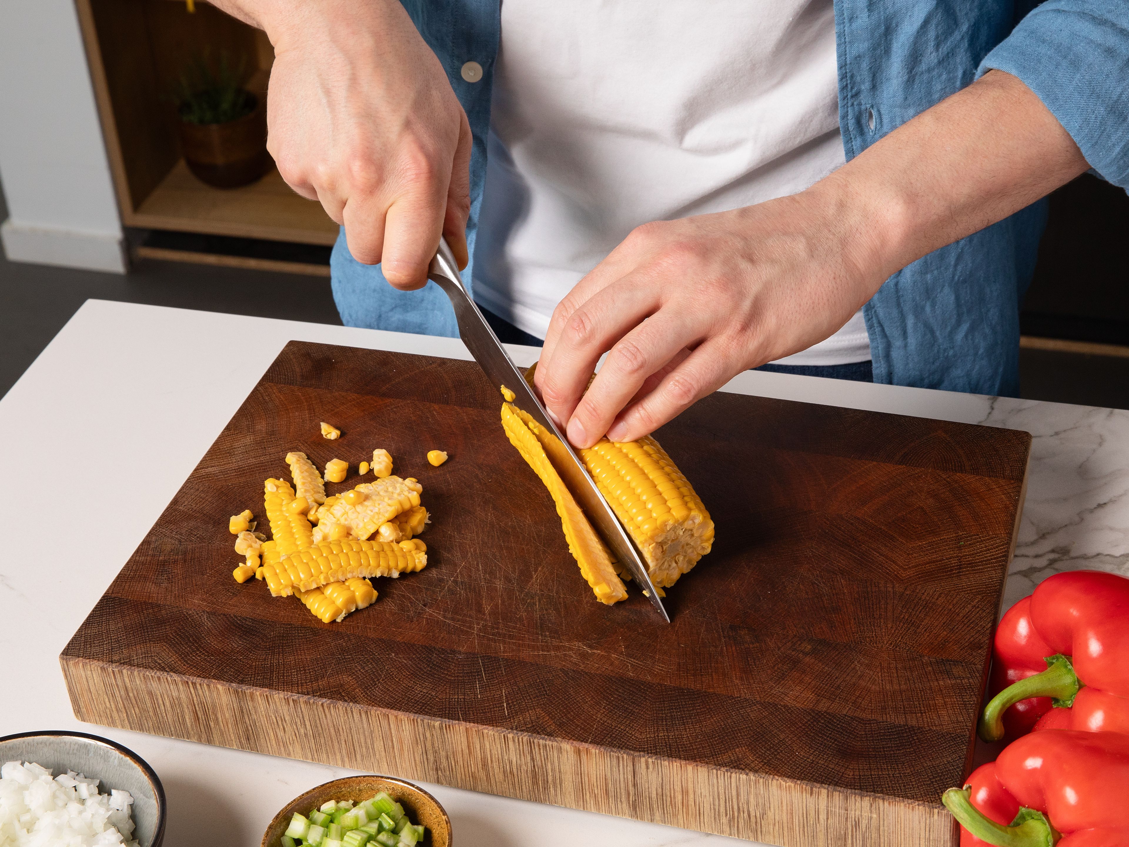 Zwiebel schälen und fein würfeln. Knoblauch schälen und fein hacken. Sellerie und Paprika in kleine Würfel schneiden. Die Körner vom Maiskolben mit einem Messer vom Strunk schneiden. Limette halbieren. Petersilie fein hacken.