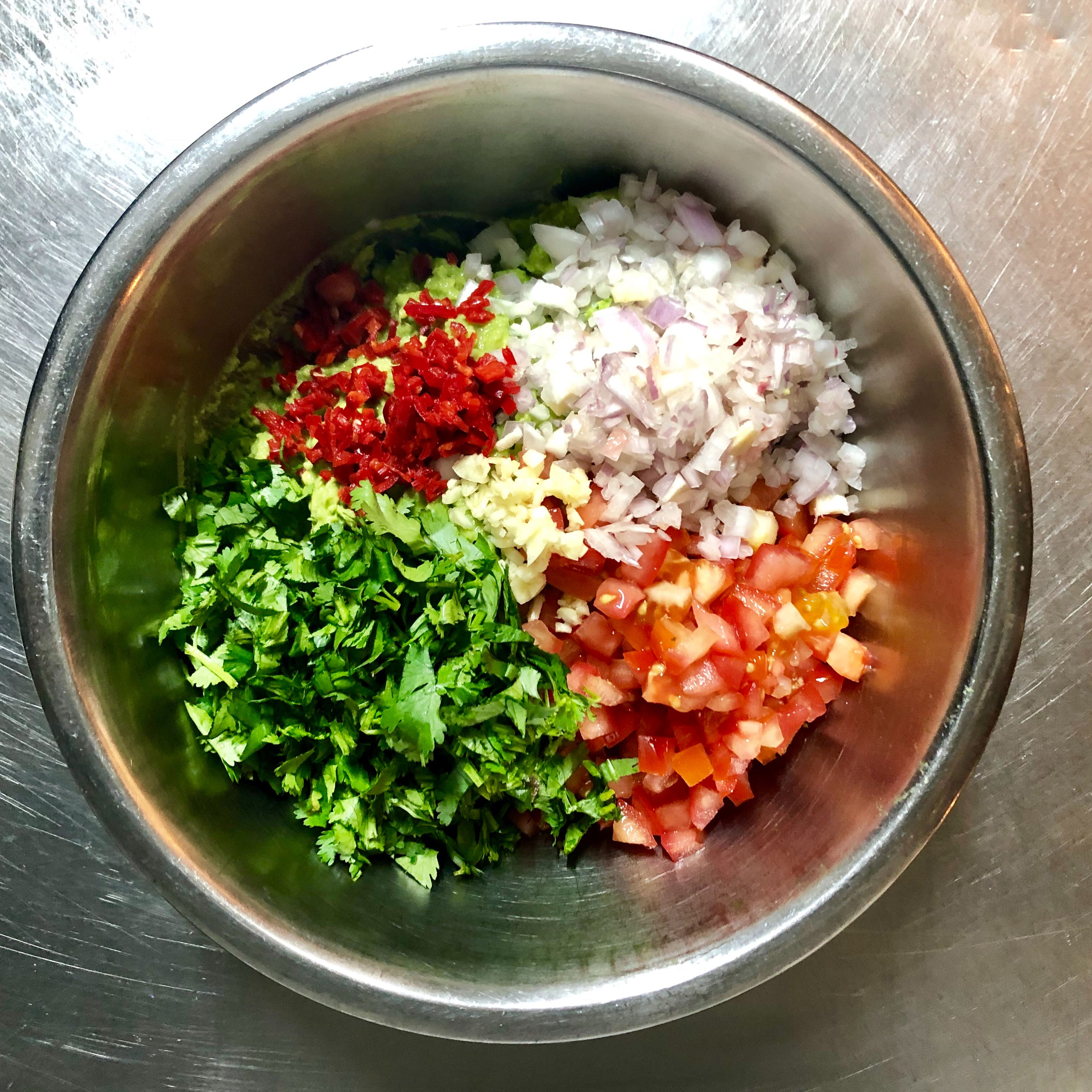 Fold in the tomatos, shallot, garlic, coriander and chili pepper. Mix everything together and let guacamole rest for 30 minutes before serving so the flavors can meld.