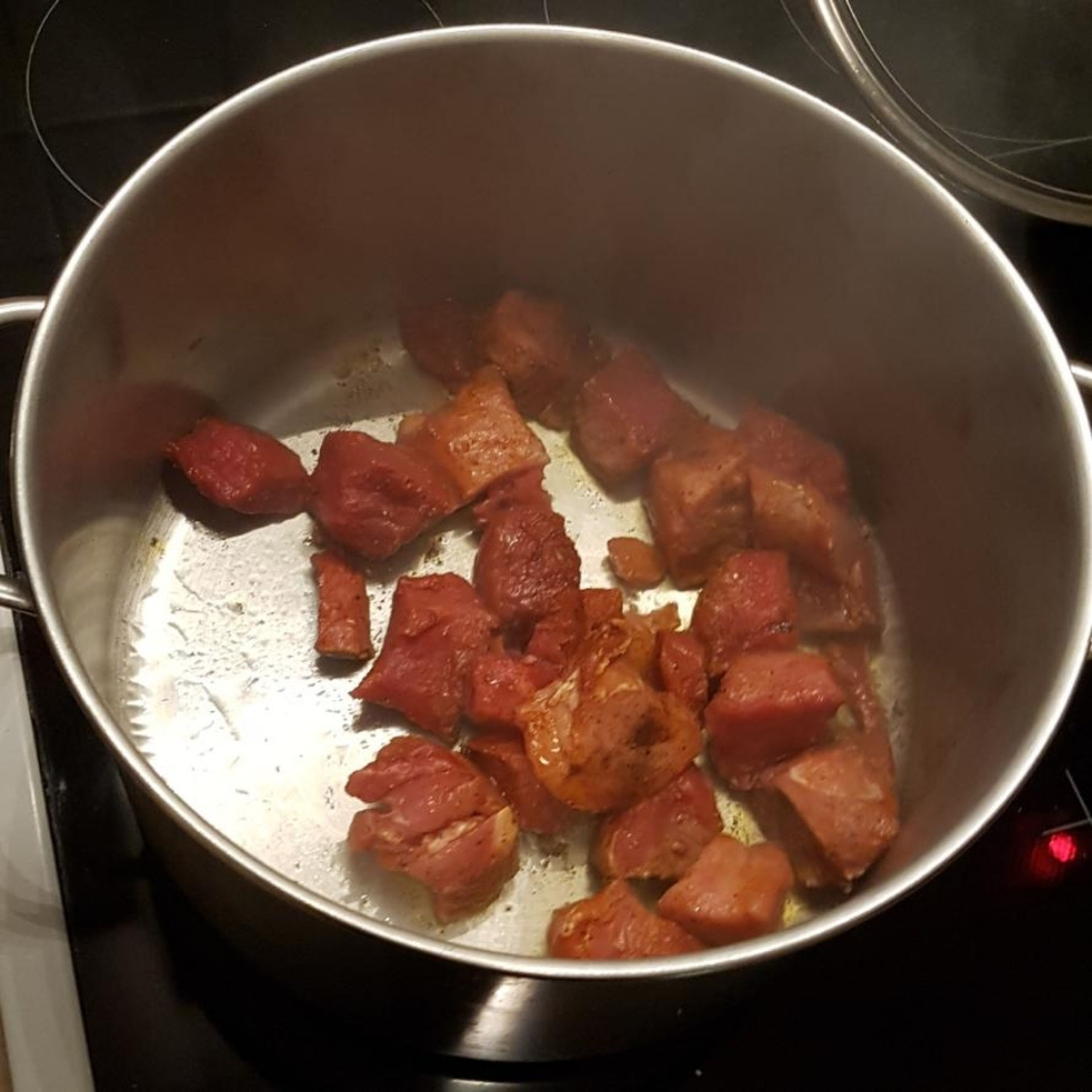 Öl in einem Topf stark erhitzen und dann das Fleisch darin rundherum scharf anbraten und dabei Tomatenmark hinzugeben. Anschließend das Fleisch aus dem Topf nehmen und beiseite stellen.