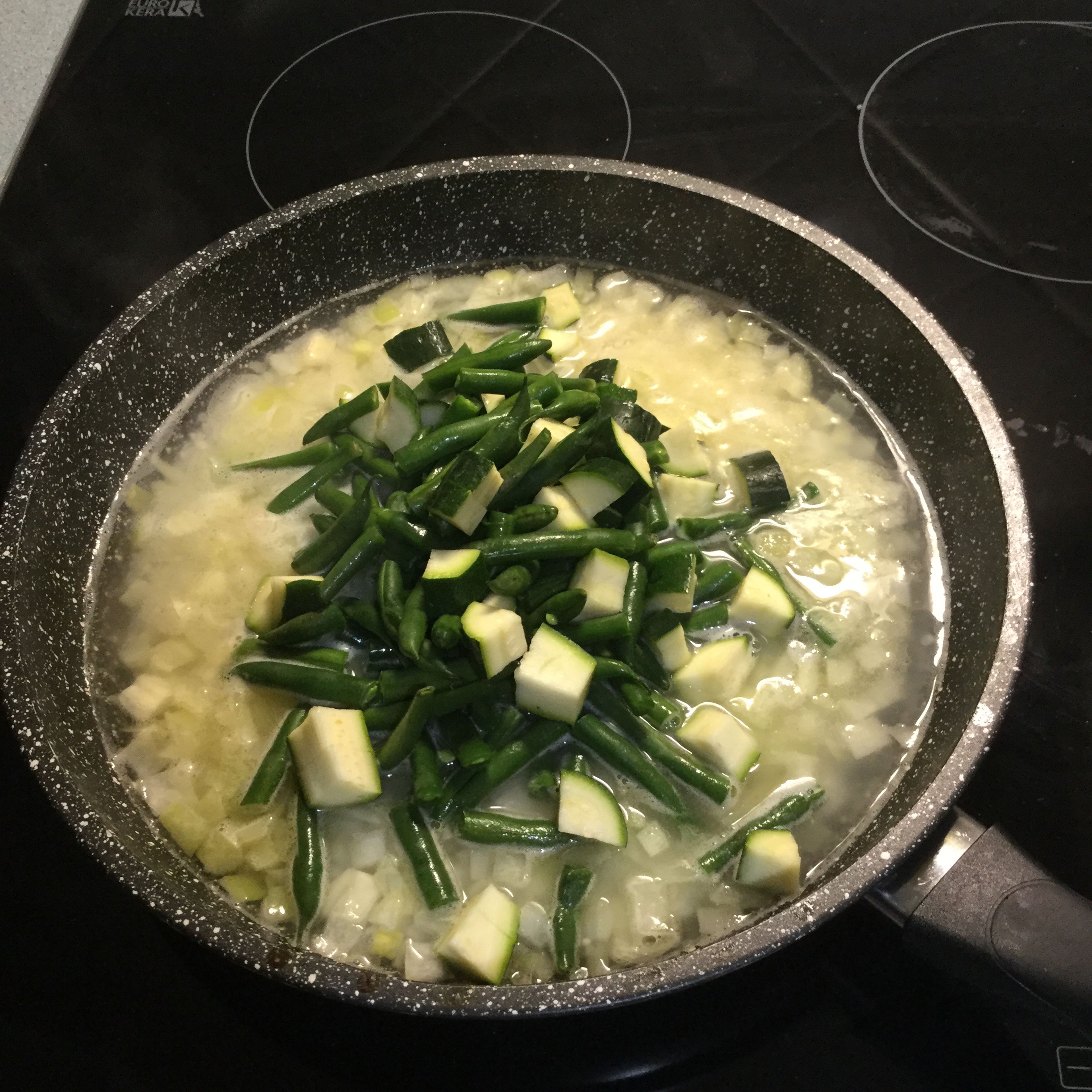 Heat a large frying pan and melt butter. Add the onion and cook until softened before adding the garlic. Add the arborio rice and stir to combine. Then, add two cups off water and leave to boil until first bubbles appear. When mixture starts boiling, add the chopped zucchini and beans.