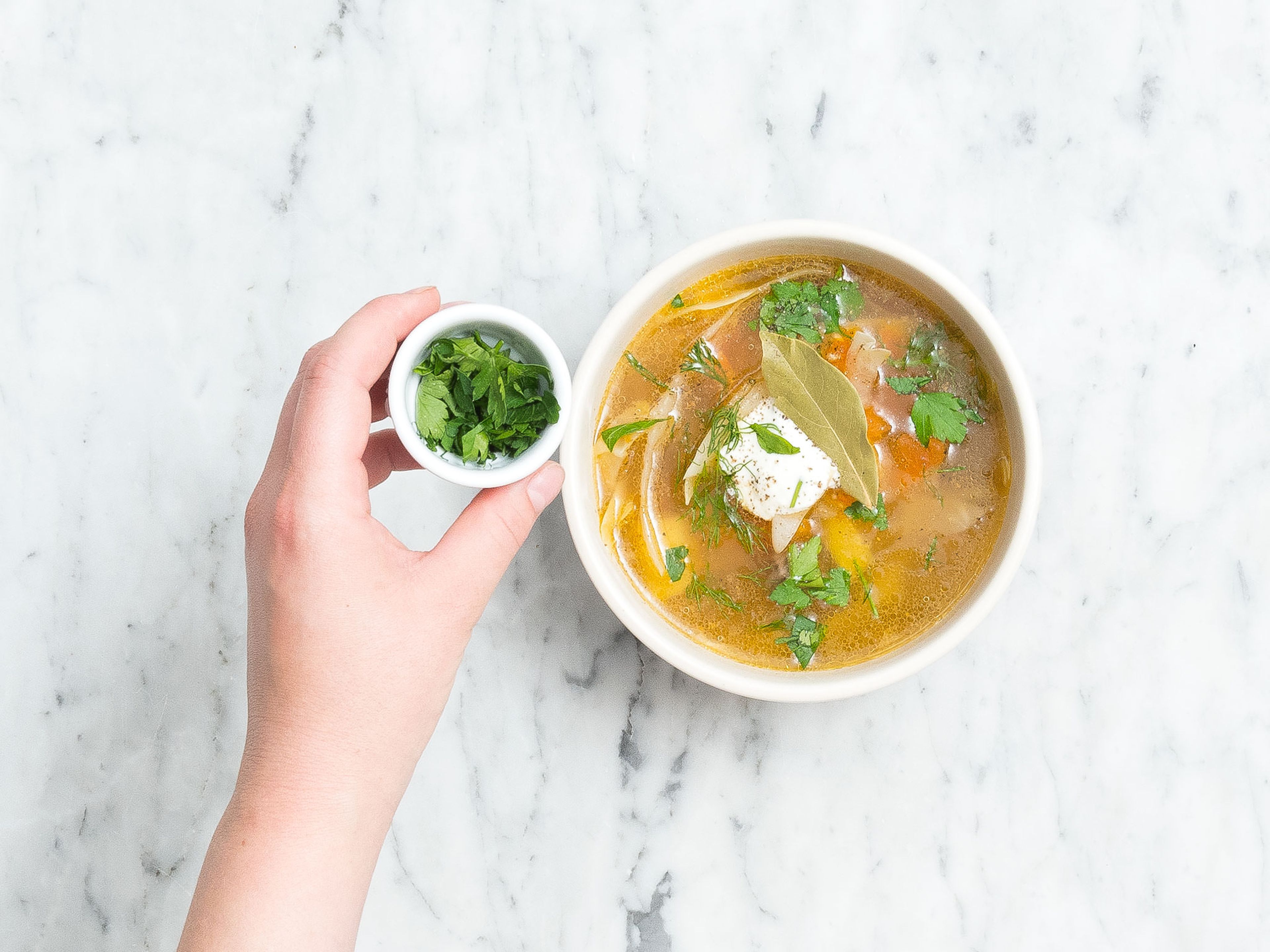 Serve cabbage soup in bowls with a dollop of sour cream, a bay leaf, dill, parsley, and season with more pepper. Enjoy!