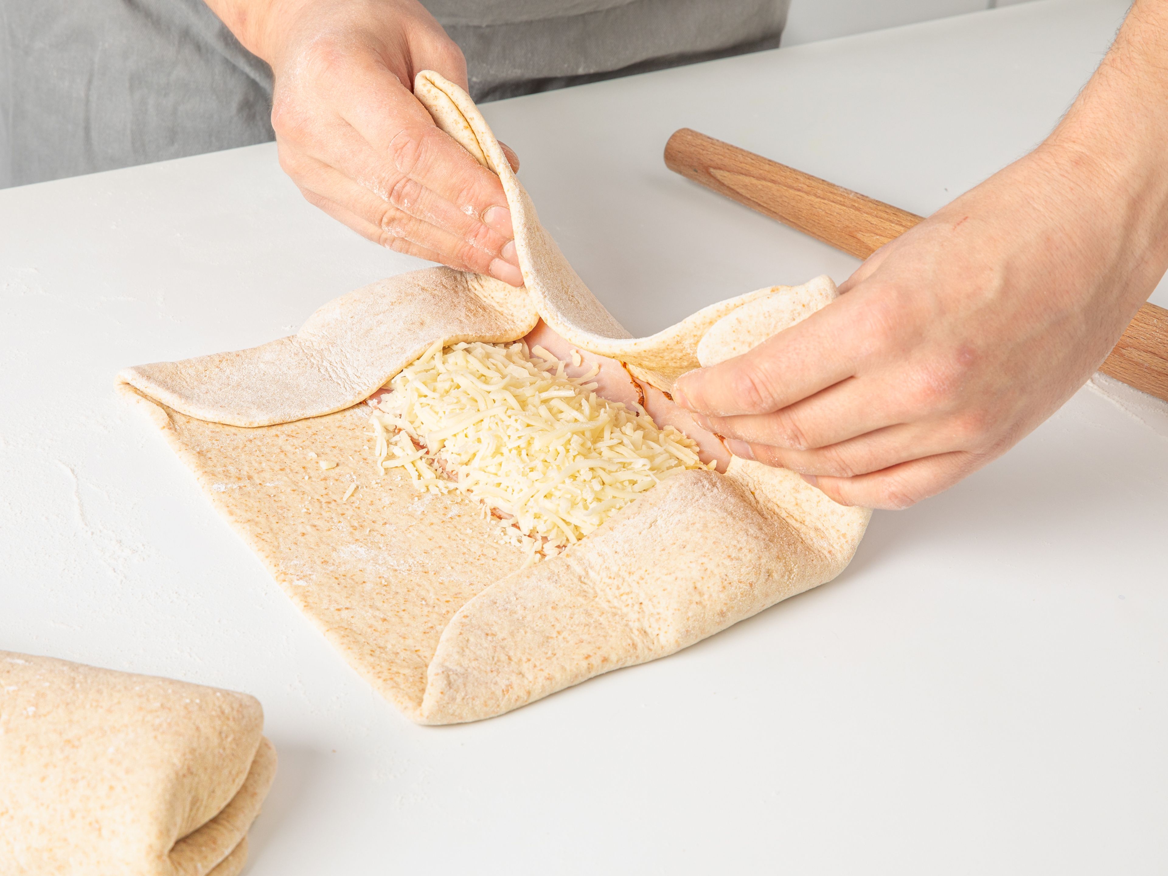Preheat the oven to 200°C/390°F. Once the dough is ready, remove it from the bowl and place it on a flour-dusted work surface. Divide the dough in half. Roll out each piece into a long rectangle. Add ham and cheese to the center of the rectangle, leaving an approx. 5 cm/2 in. edge. Start by folding the two short sides inwards over the filling, then carefully fold the two long sides over to seal it. Turn the filled pastry roll, so that the seam side is facing down.