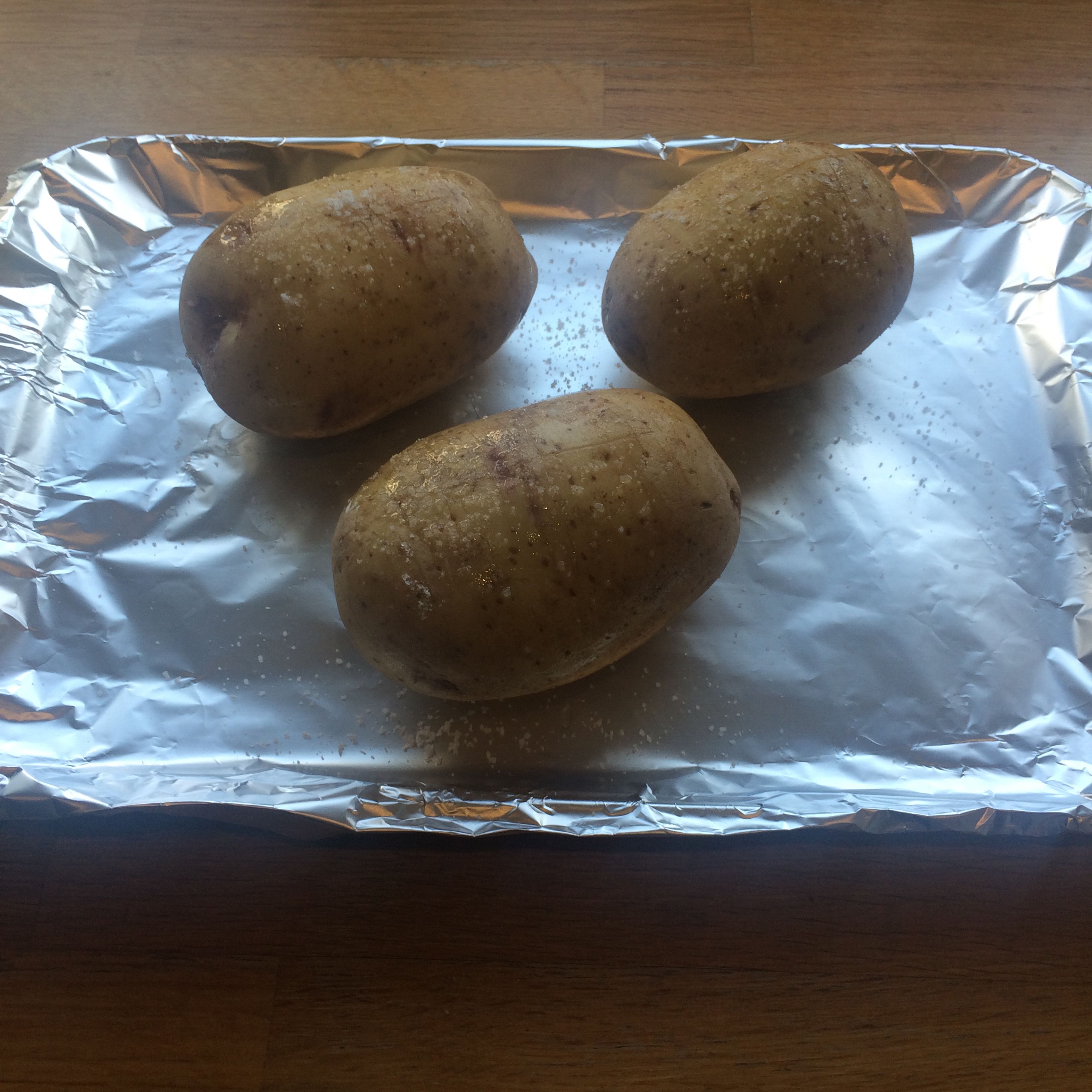 Preheat oven to 220°C and prepare potatoes by piercing all over with a butter knife and then score a cross on the top. Rub a teaspoon of oil onto each potato and grind over plenty of salt. Place in the oven and leave to cook for 1 hour
