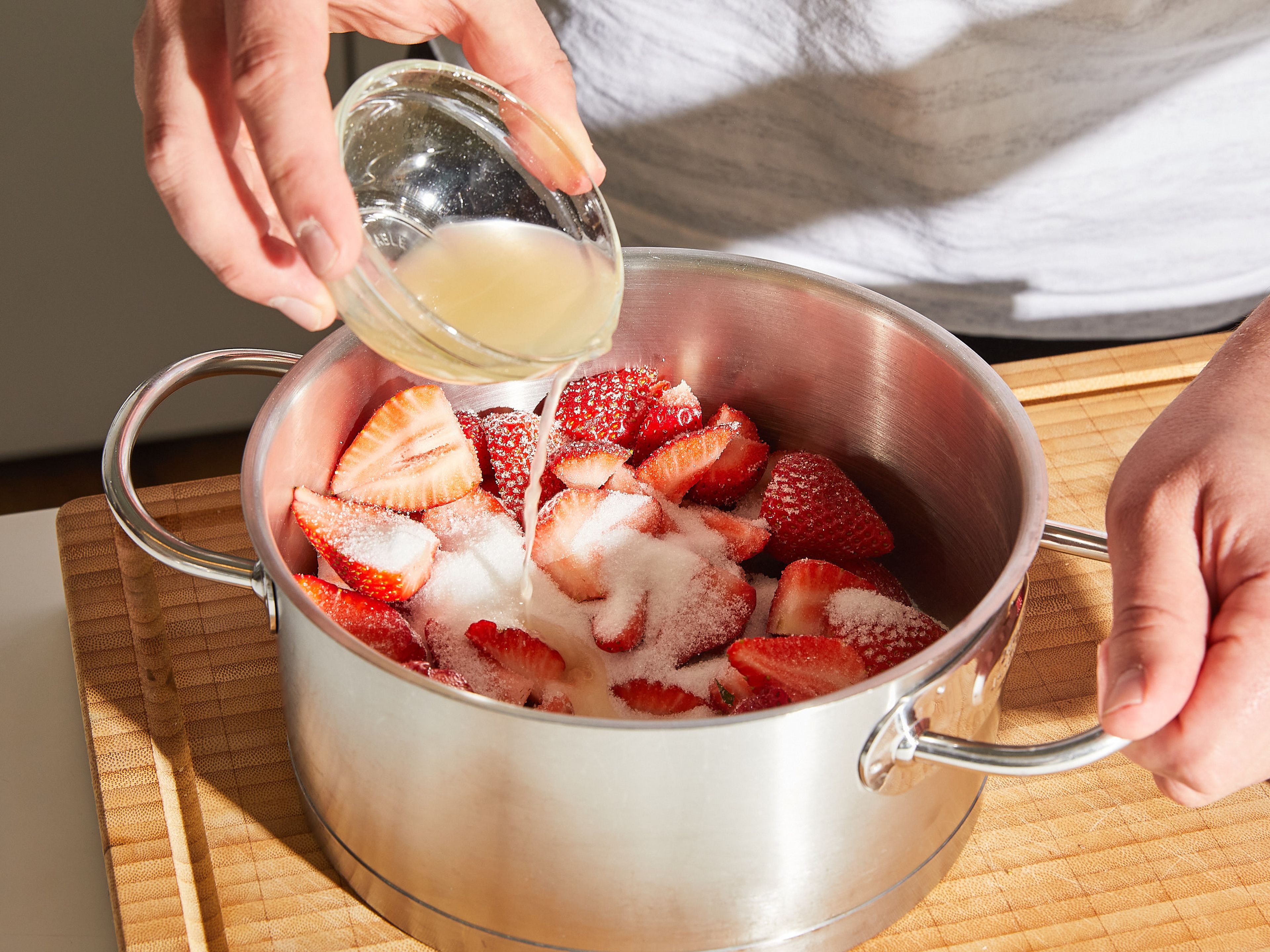 Erdbeeren vom Strunk befreien und vierteln, dabei einige ganze Erdbeeren zum Servieren aufbewahren. Die Erdbeeren in einen Topf geben und mit Zucker und Zitronensaft vermischen. Anschließend beiseite stellen.