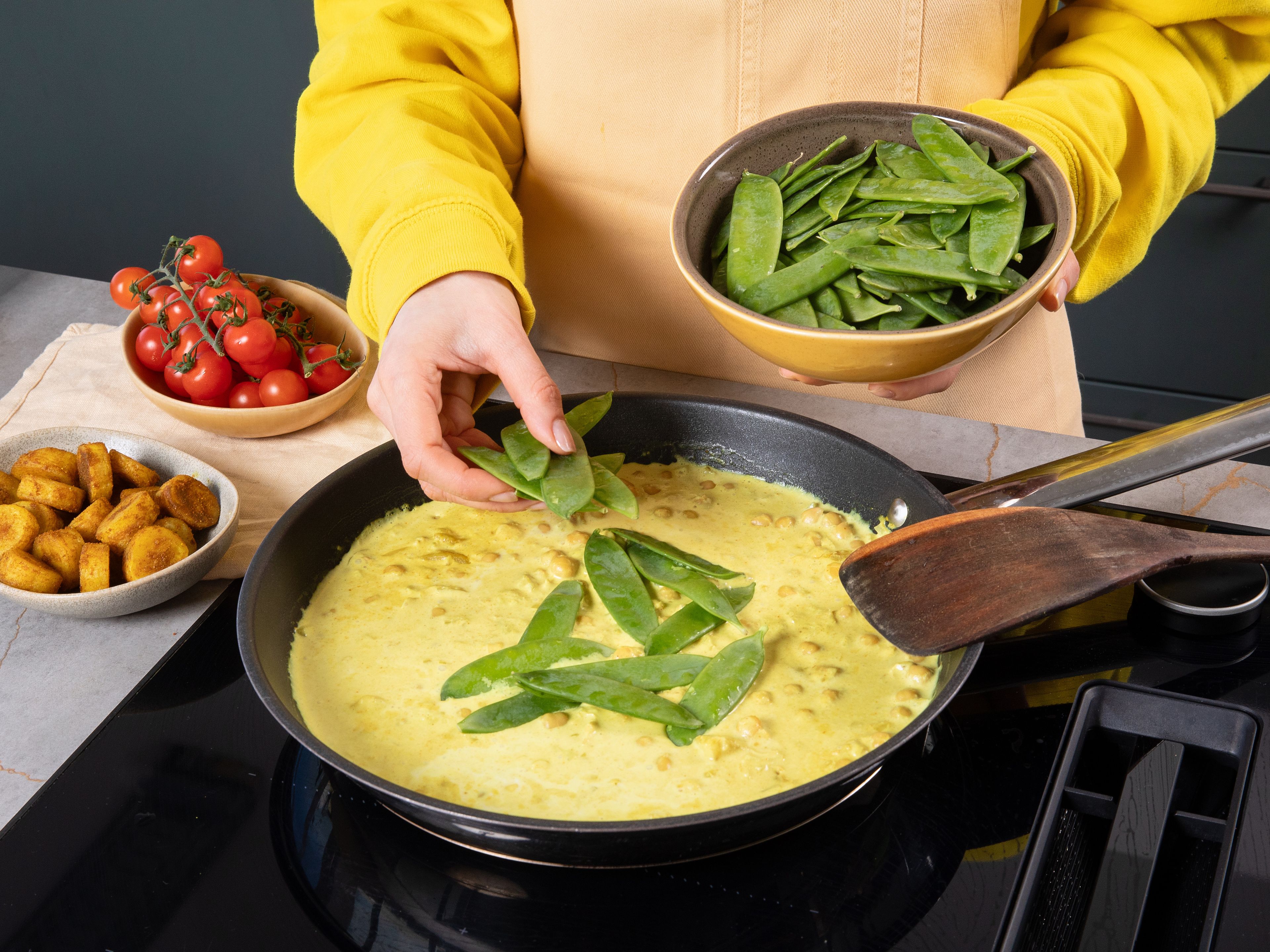 Erneut etwas Öl in die zuvor verwendete Pfanne geben und Zwiebel darin ca. 2–3 Min. glasig dünsten, dann Ingwer und Knoblauch zugeben und kurz mitbraten. Mit Kokosmilch ablöschen, Kichererbsen und ⅔ der Bananen einrühren. Ca. 5 Min. sanft köcheln lassen. Cherrytomaten und Zuckerschoten zugeben und ca. 3–4 Min. weiter köcheln lassen. Mit Salz, dem restlichen Currypulver und Limettensaft abschmecken.