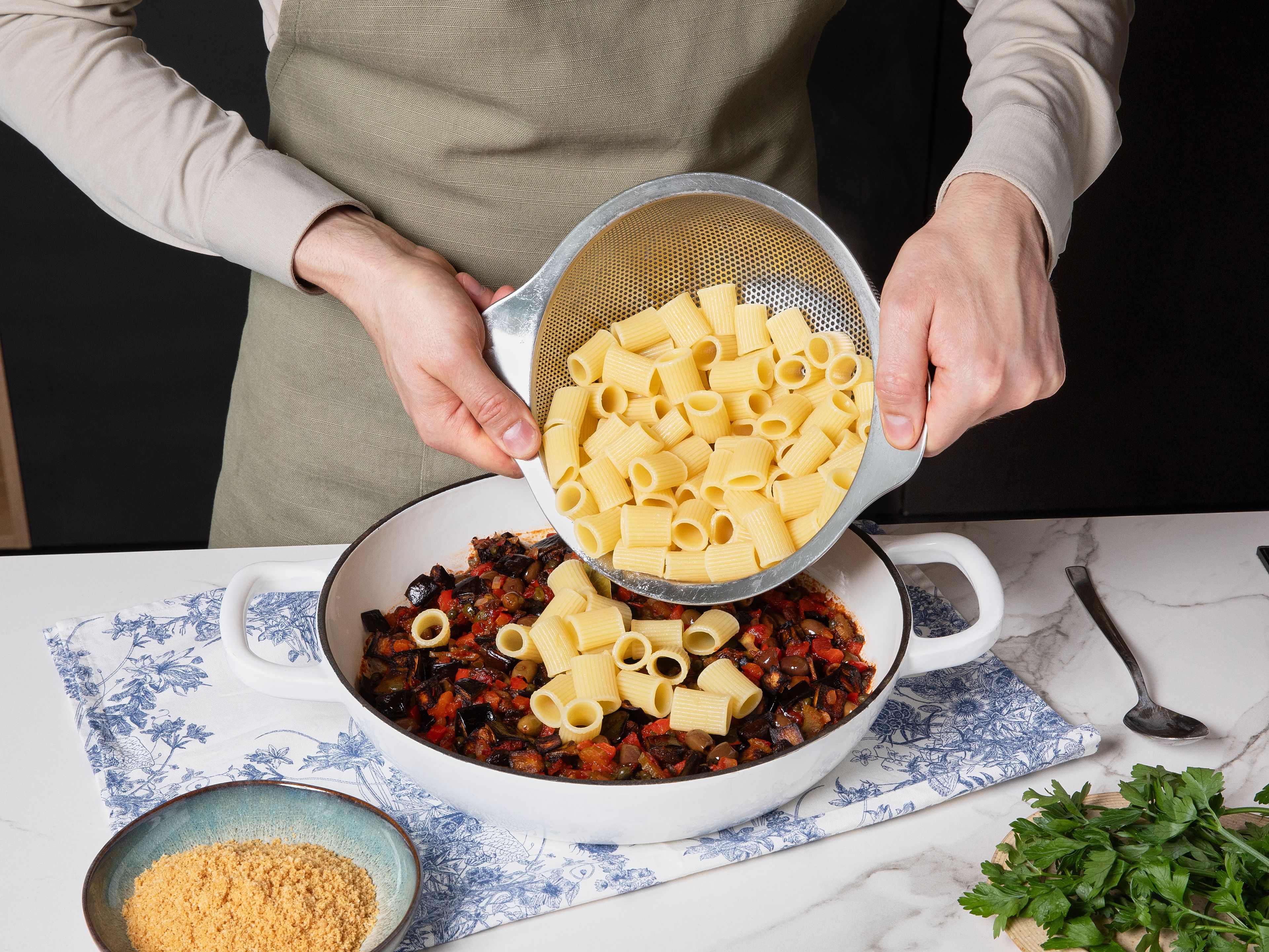Die Mezzi Rigatoni in einem großen Topf mit Salzwasser nach Packungsanleitung al dente kochen, dann abgießen. Die Pasta mit der Caponata vermengen, nach Bedarf etwas Kochwasser hinzufügen. Auf Tellern anrichten, mit frischer Petersilie garnieren und das knusprige Parmesan-Topping darüberstreuen.