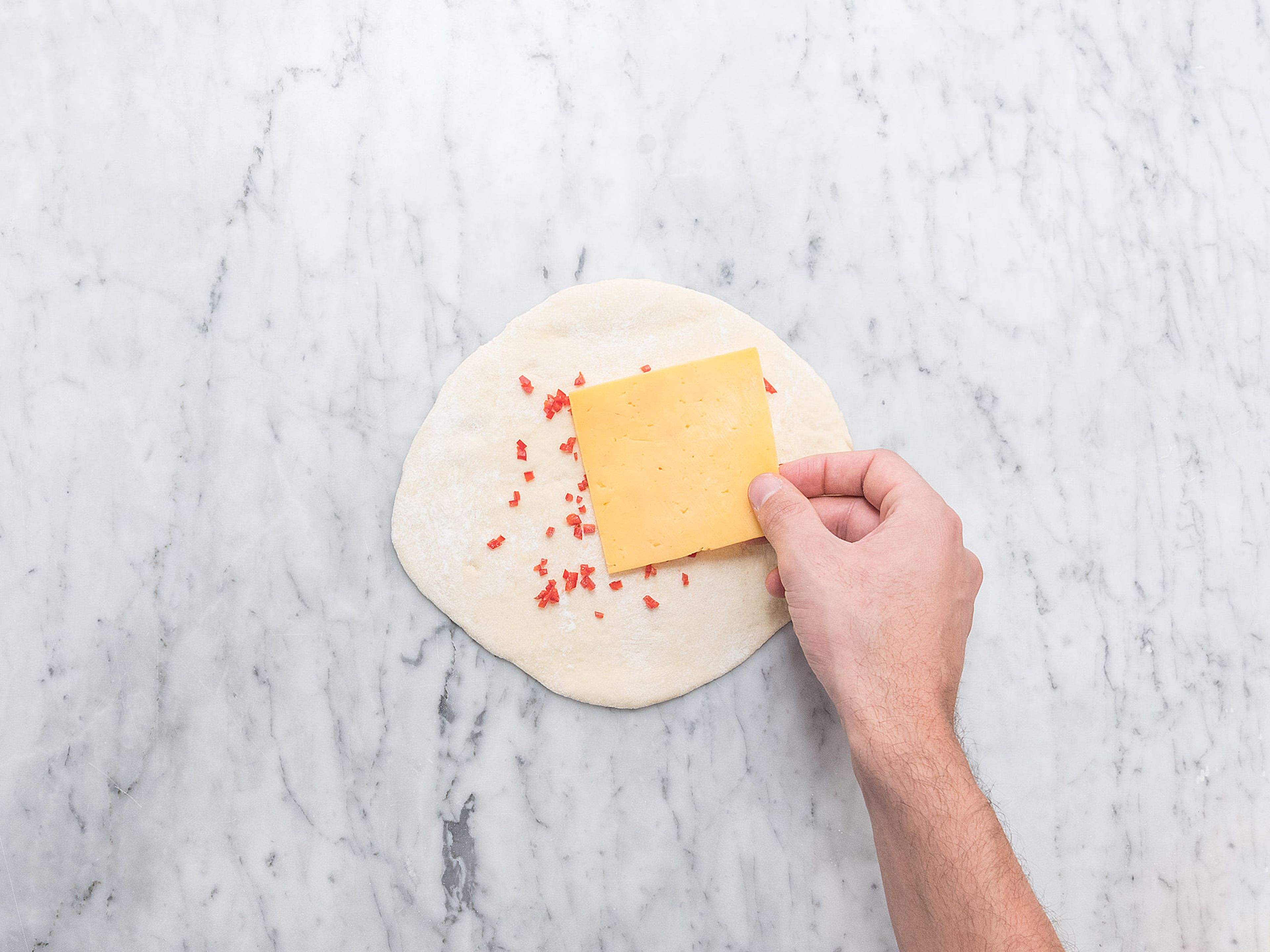 Chili hacken und jeweils auf dem Teig verteilen. Mit Cheddarkäse belegen, dabei einen Rand von ca. 2 cm frei lassen. Mit einem weiteren Stück Teig bedecken und die Ränder aneinander drücken und verschließen, damit der Käse nicht herausfließen kann.