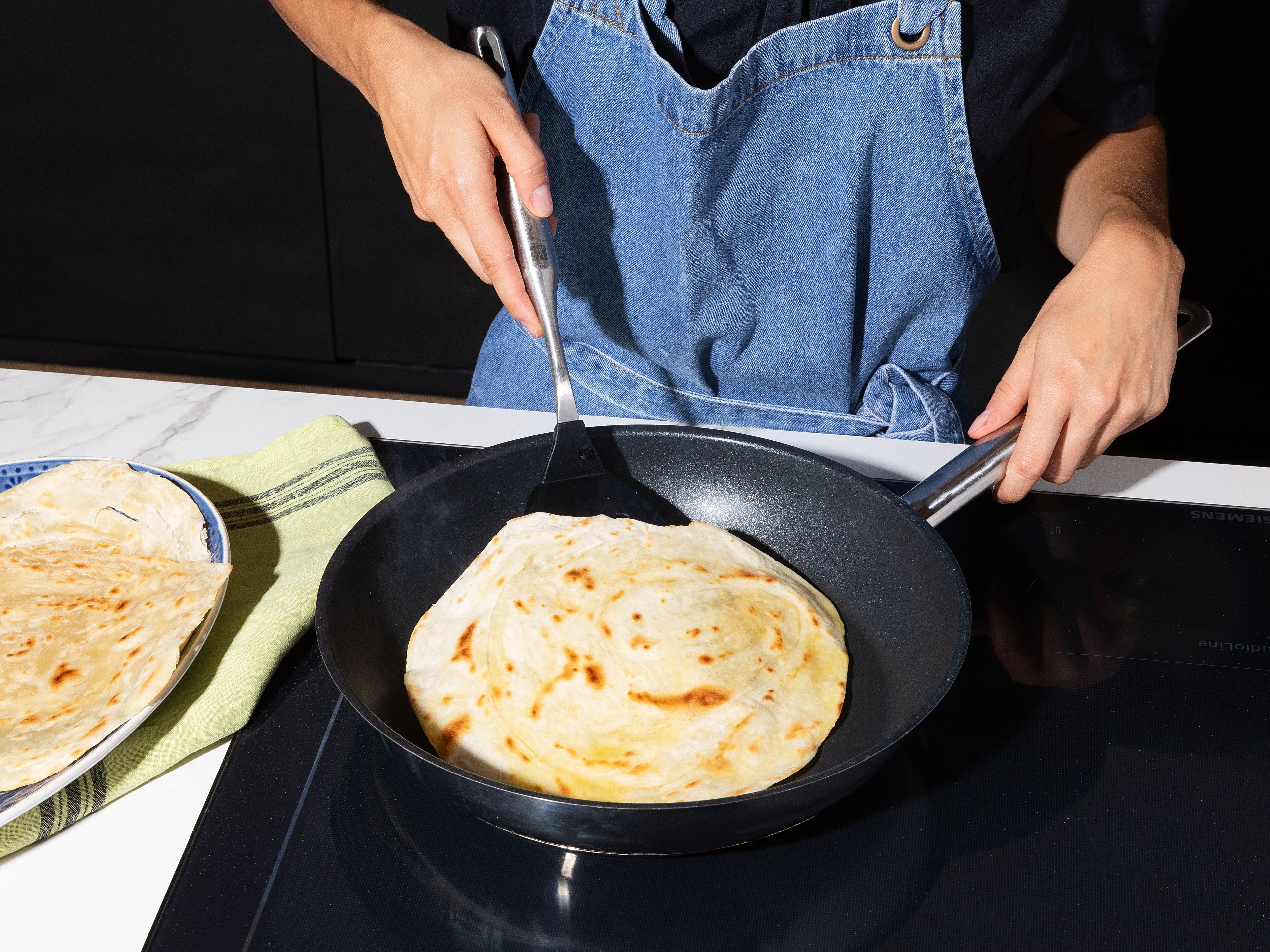 Die Hälfte der Brote ausgerollt zwischen Schichten aus Backpapier legen und roh einfrieren, die restlichen Brote nacheinander in einer heißen Pfanne ca. 2 Min. pro Seite ausbacken, bis sie leicht durchsichtig sind, aufpuffen und sich die typischen Schichten bilden, dabei von jeder Seite nochmals mit etwas Ghee bestreichen. Die Kichererbsen auf den Paratha-Broten verteilen und etwas Minzsoße darübergeben. Die eingelegten Zwiebeln aus der Flüssigkeit nehmen und mit dem übrigen Koriander vermengen. Die Wraps mit dem Koriander-Salat toppen und sofort servieren.