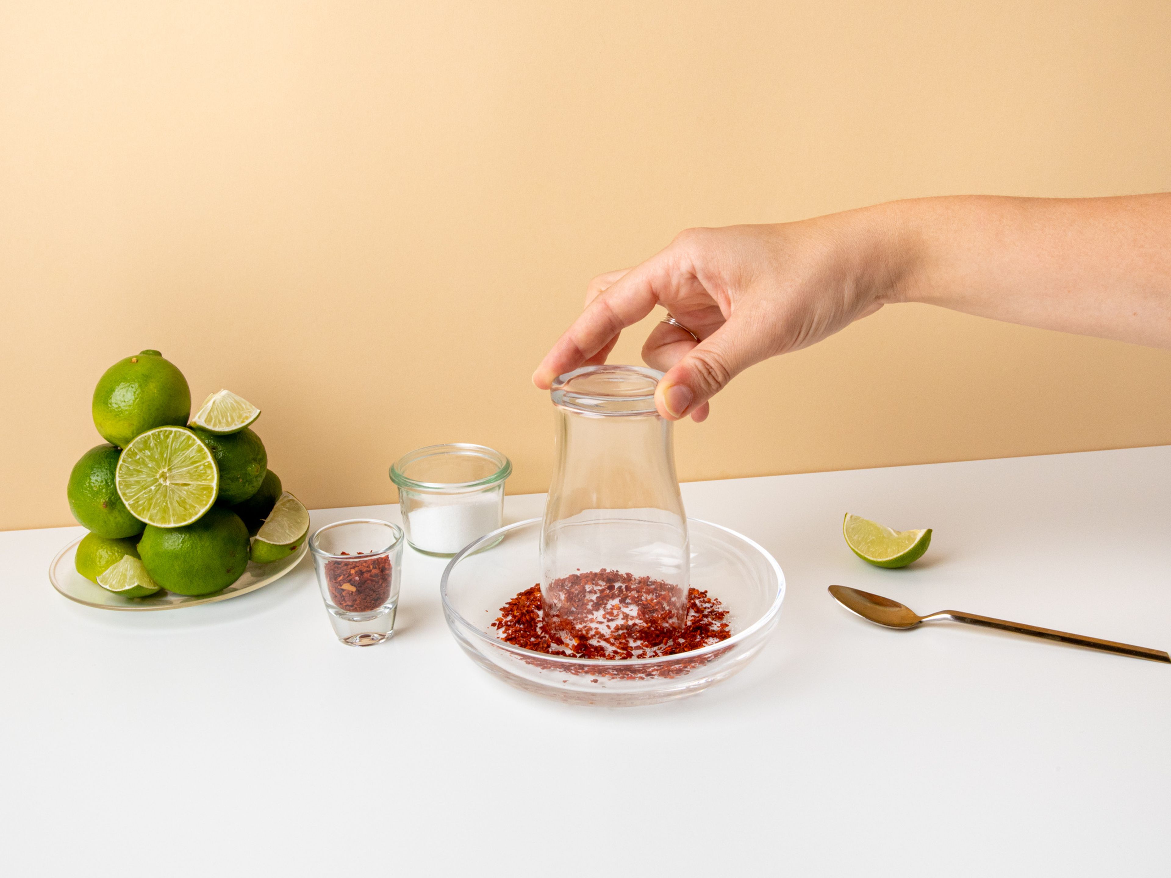 Add chili flakes, sugar, and salt to a small plate. Mix well. Halve one of the limes and rub one half around the rim of the glass. Turn glass upside down and swivel it so the rim becomes coated in the chili mixture.