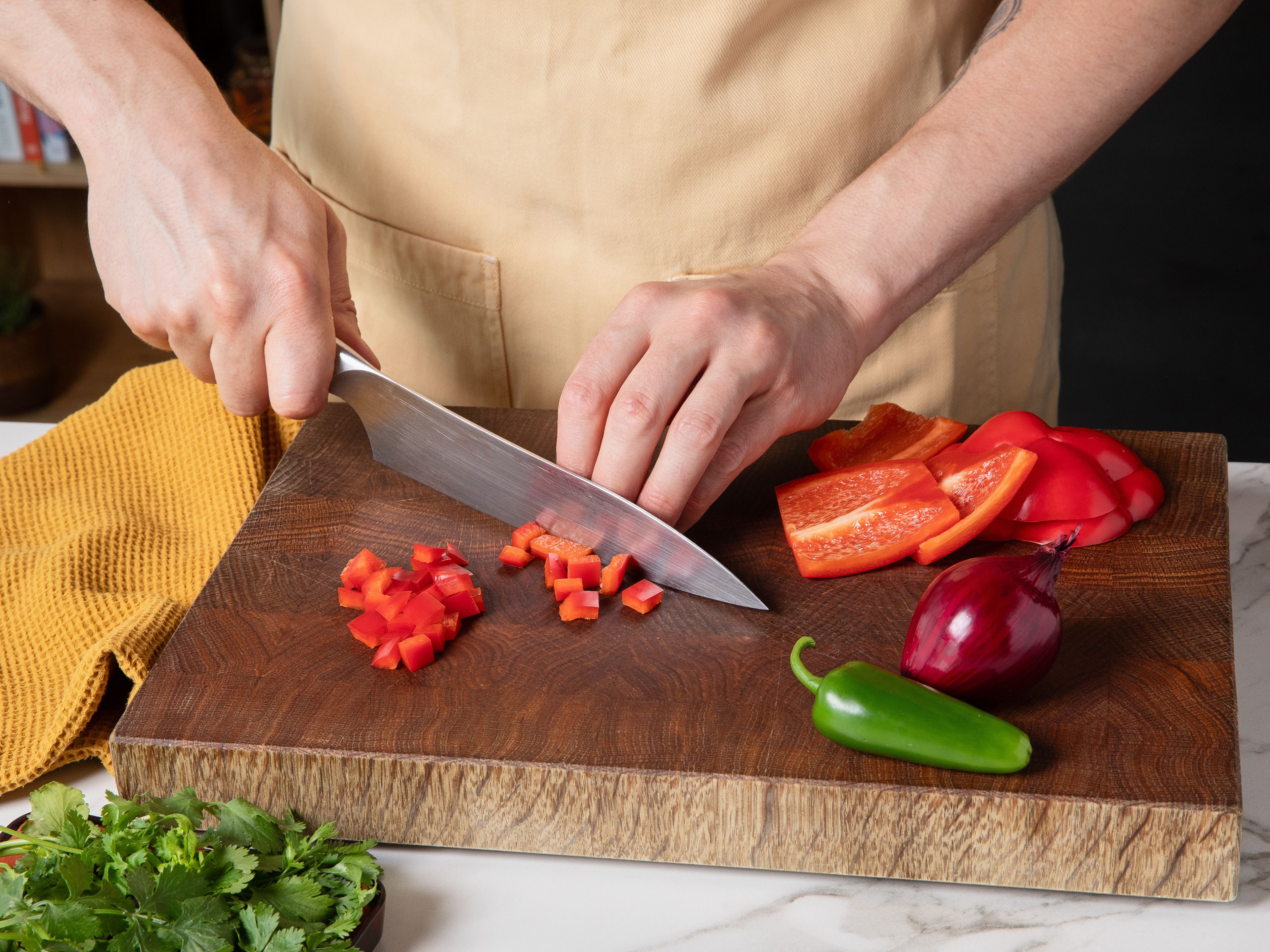 Den Ofen auf 200 °C Ober-/Unterhitze vorheizen. Die Paprika entkernen und in kleine Würfel schneiden. Die Zwiebel schälen und fein würfeln. Koriander grob hacken. Jalapeño längs halbieren, entkernen und in feine Würfel schneiden.