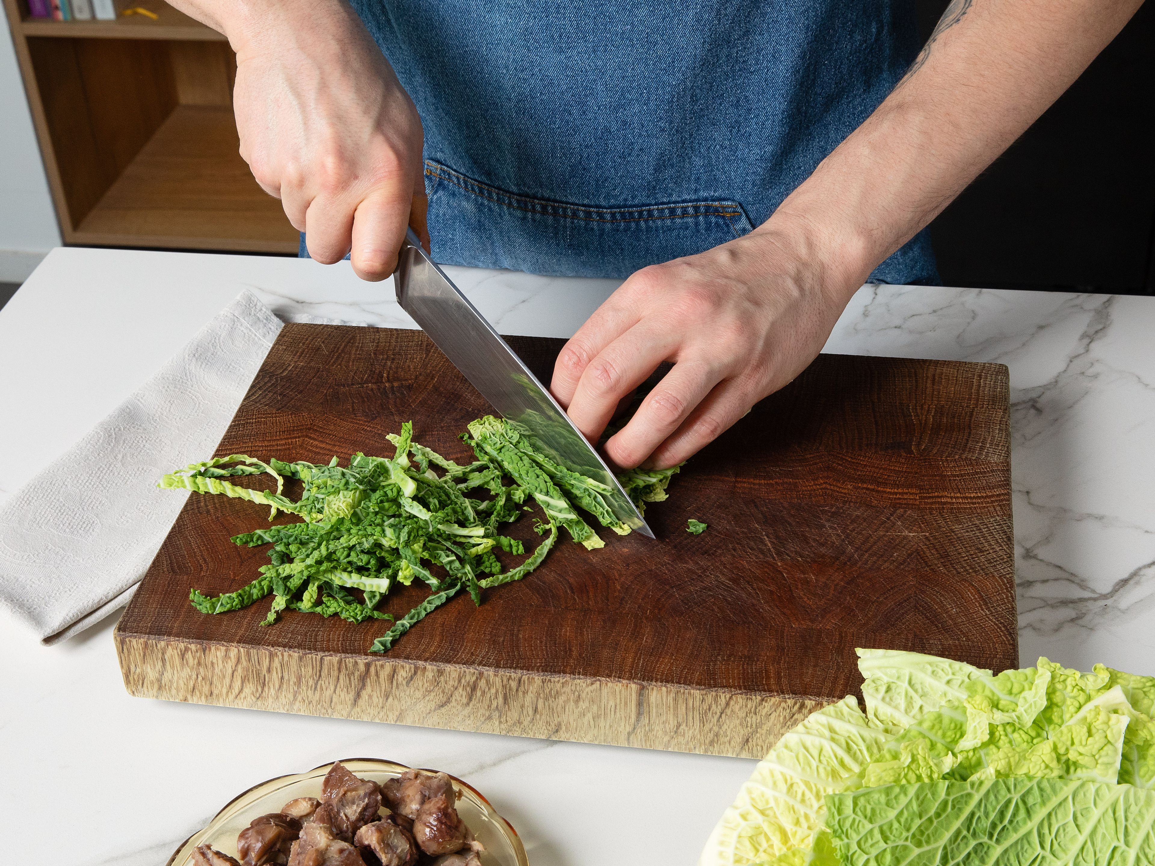 Einen großen Topf mit Salzwasser zum Kochen bringen und die Spaghetti darin nach Packungsanweisung al dente garen. Nach Ende der Kochzeit ca. 120 ml des Kochwassers beiseite stellen, den Rest abgießen. Währenddessen den Wirsing in feine Streifen schneiden, die Maronen grob hacken und den Knoblauch schälen und fein hacken.