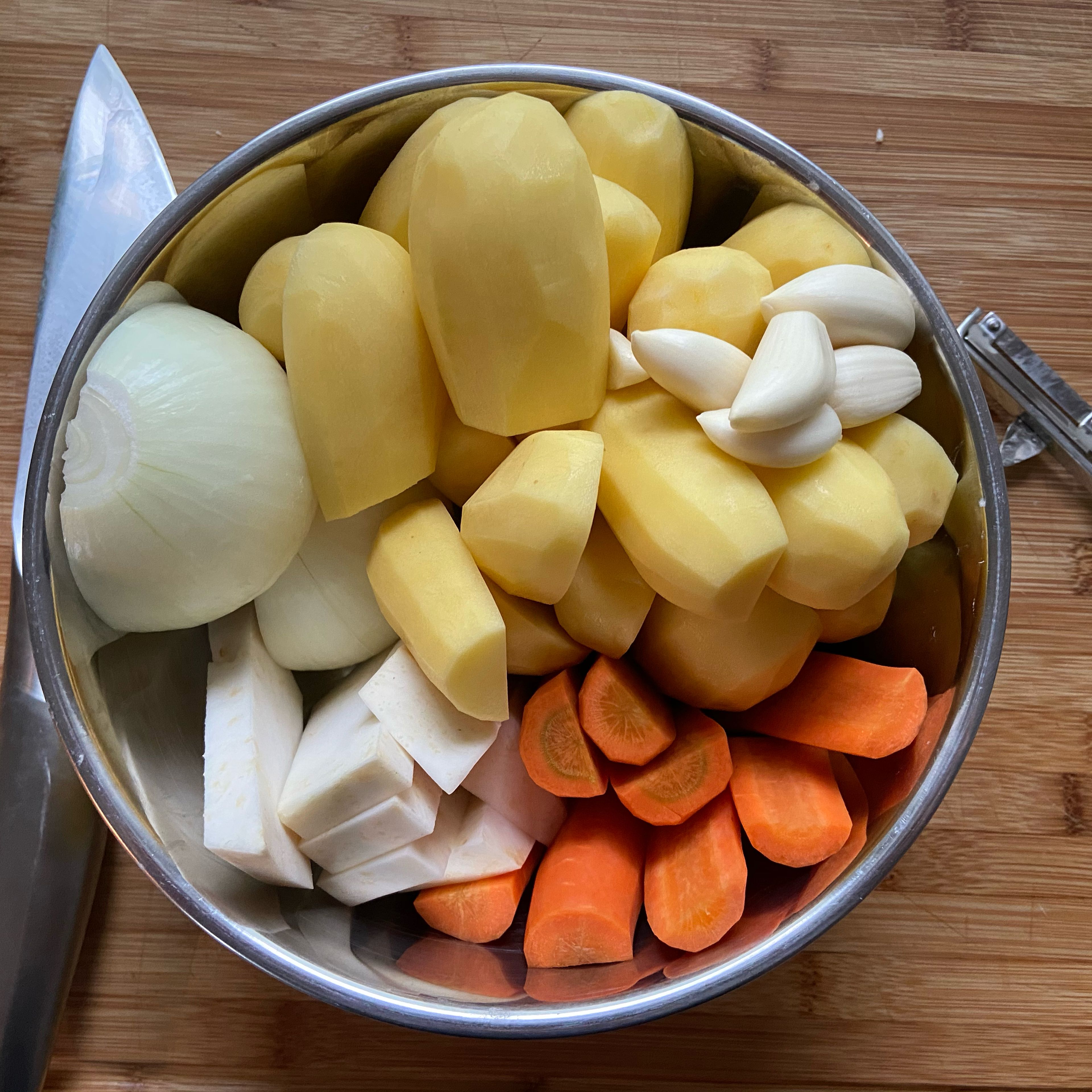 Eine Zwiebel und die Kartoffeln halbieren, die Karotten in halbe Hälften schneiden und den Sellerie in ähnlich große Stücke schneiden.