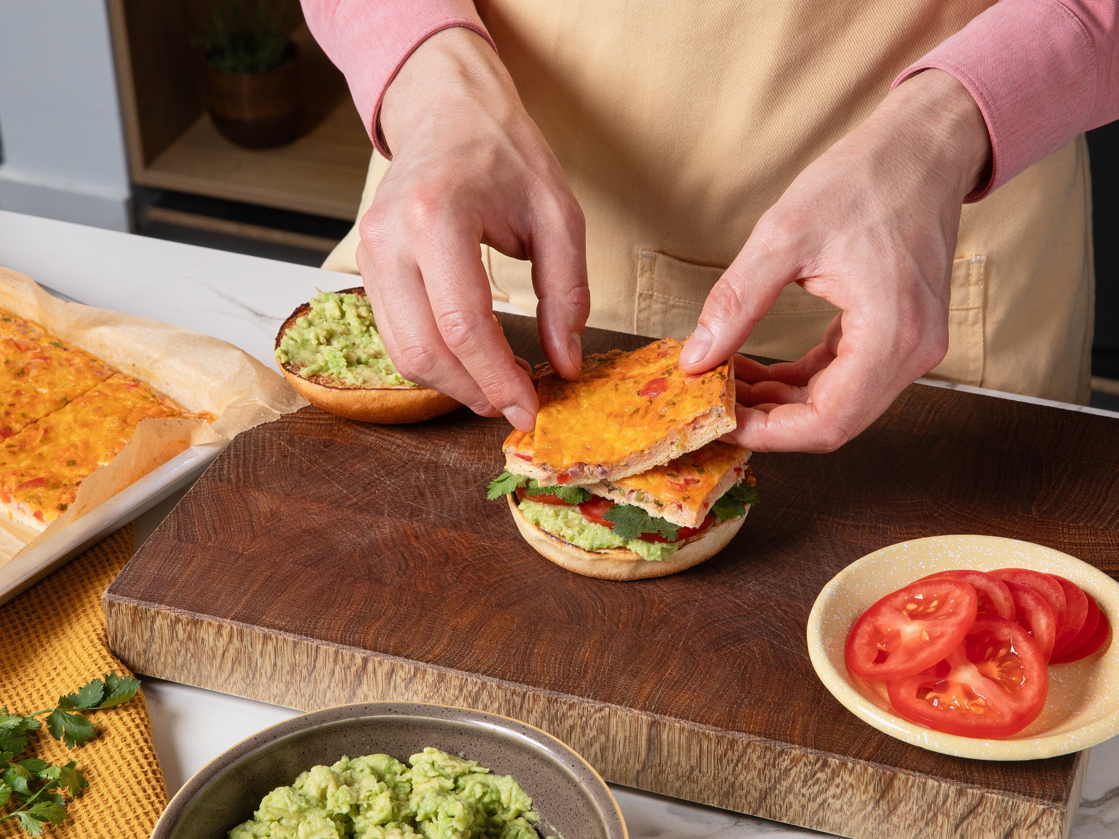 Die Brioche-Brötchen mit der Schnittfläche in einer Pfanne ohne Fett ca. 2–3 Min. anrösten, bis sie leicht gebräunt sind. Anschließend die Unterseiten mit der Avocadocreme bestreichen und mit Tomatenscheiben belegen. Das gebackene Ei in 8 rechteckige Stücke schneiden. Je zwei Stück auf die vorbereiteten Bun-Unterseiten legen, mit dem restlichen Koriander bestreuen und die obere Brötchenhälfte darauf setzen. Mayonnaise und scharfe Soße darauf geben und sofort servieren.