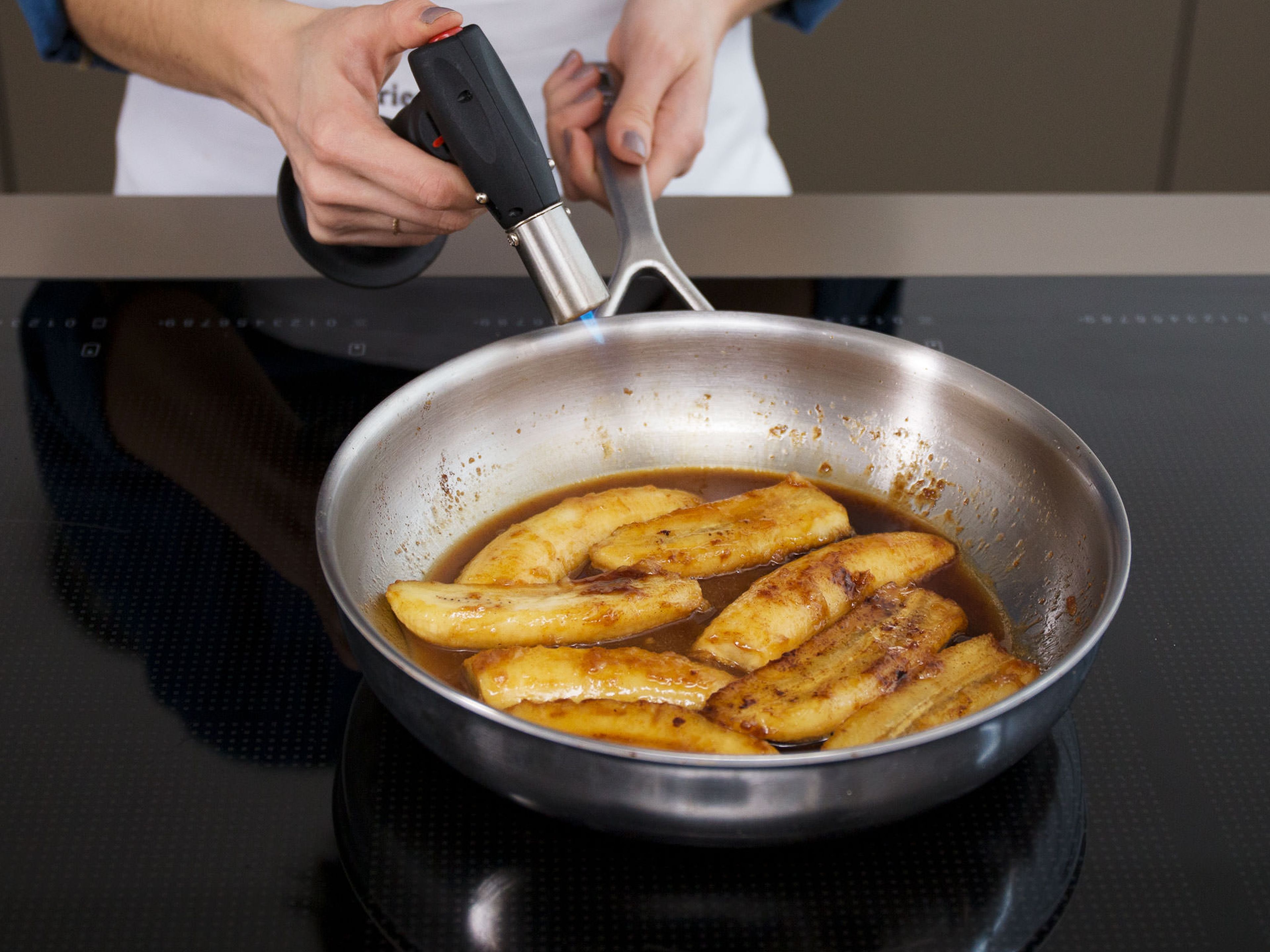 Add rum to the pan. Carefully flambé the sauce with a flambé torch. Gently toss the bananas in the flaming sauce until the flame goes out. Remove the bananas from the pan and heat the sauce over medium heat, whisking until it reduces to a thick caramel consistency.