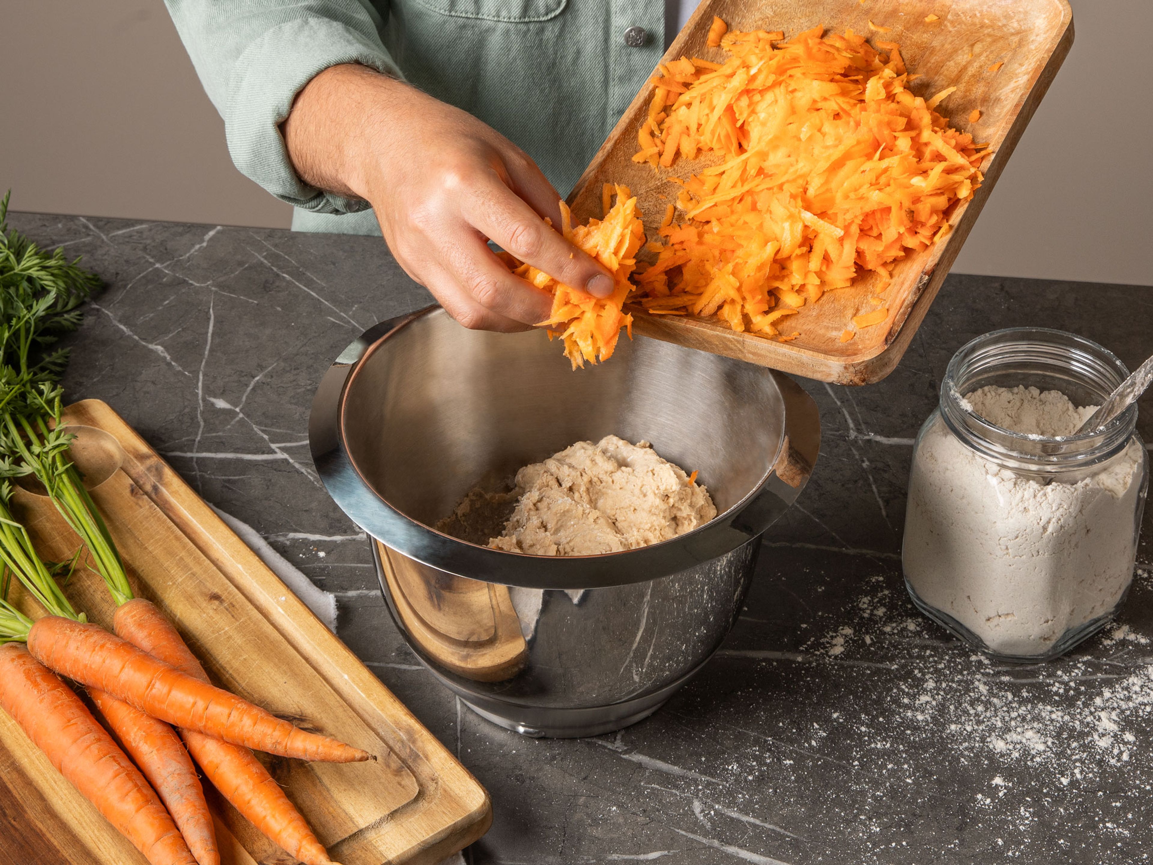 Mehl und Salz in der Schüssel einer Küchenmaschine mit Knethaken mischen. Auf niedriger Stufe rühren lassen und langsam die Hefe-Wasser-Mischung hineingeben. Kurz bevor die Zutaten vollständig in den Teig eingearbeitet sind, geraspelte Karotten hinzugeben. Küchenmaschine auf hohe Geschwindigkeit stellen und ca. 7-10 Min. kneten lassen, bis der Teig glatt und elastisch ist. Anschließend mit einem feuchten Geschirrtuch abdecken und ca. 1-2 Std. ruhen lassen, bis sich die Größe des Teigs verdoppelt hat.