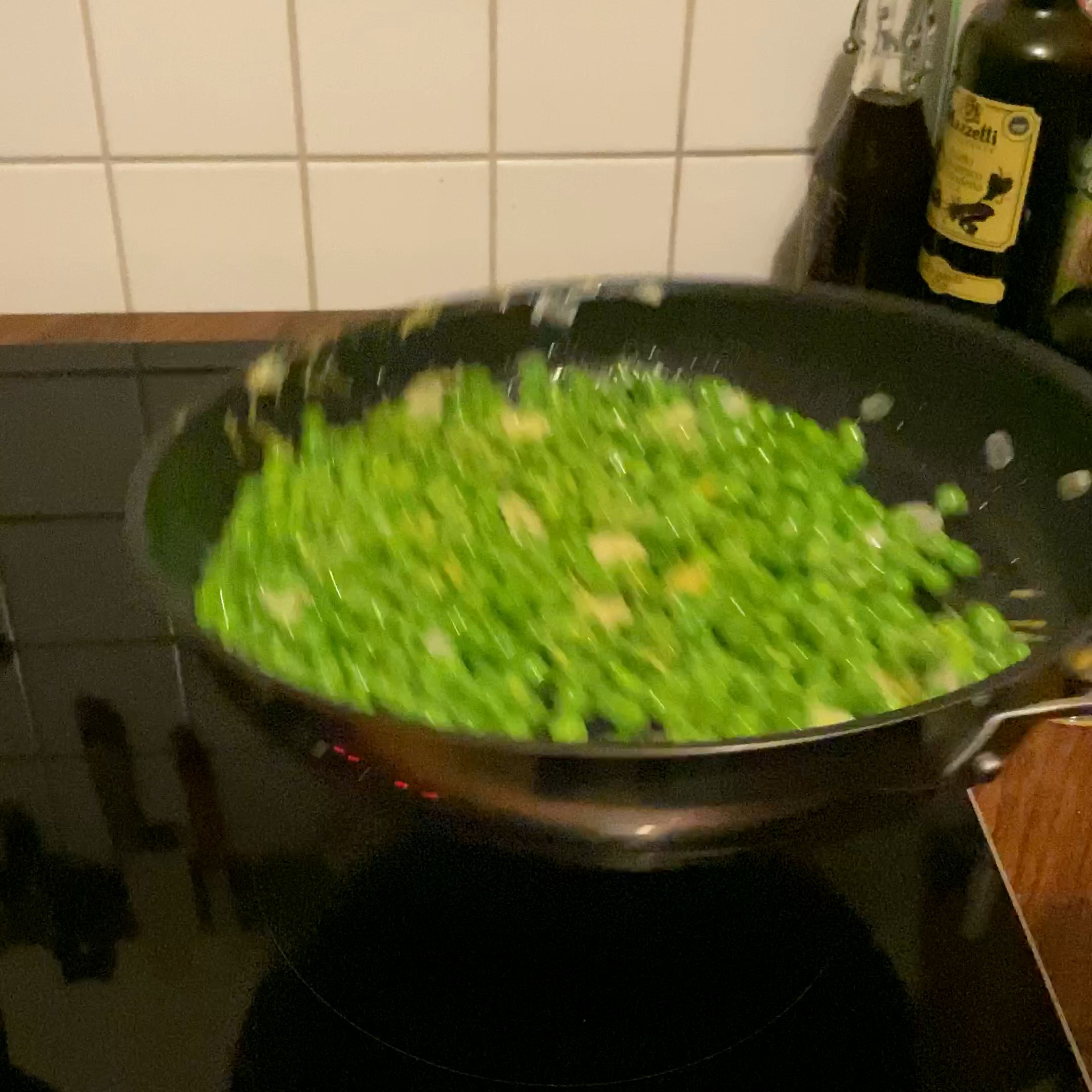 Olivenöl in einer Pfanne mit hohem Rand erhitzten und die Knoblauchscheiben darin anschwitzen. Die gefrorenen Erbsen hinzufügen und anschließend den Zitronenabrieb in die Pfanne geben. Alles gut durchmischen.