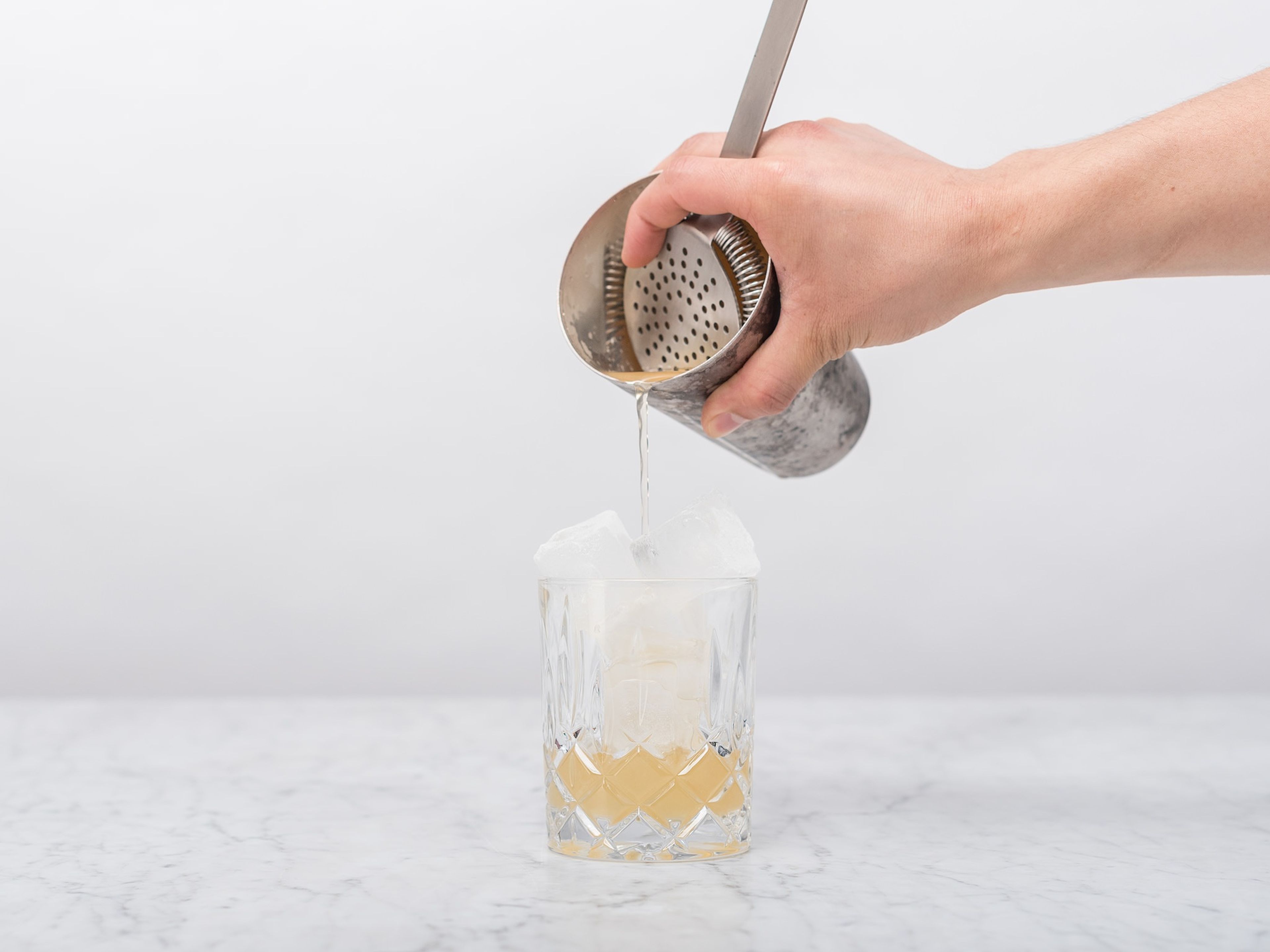 Den Cocktailshaker kräftig schütteln. Eiswürfel in ein Trinkglas füllen und den Cocktail aus dem Shaker ins Glas seihen.